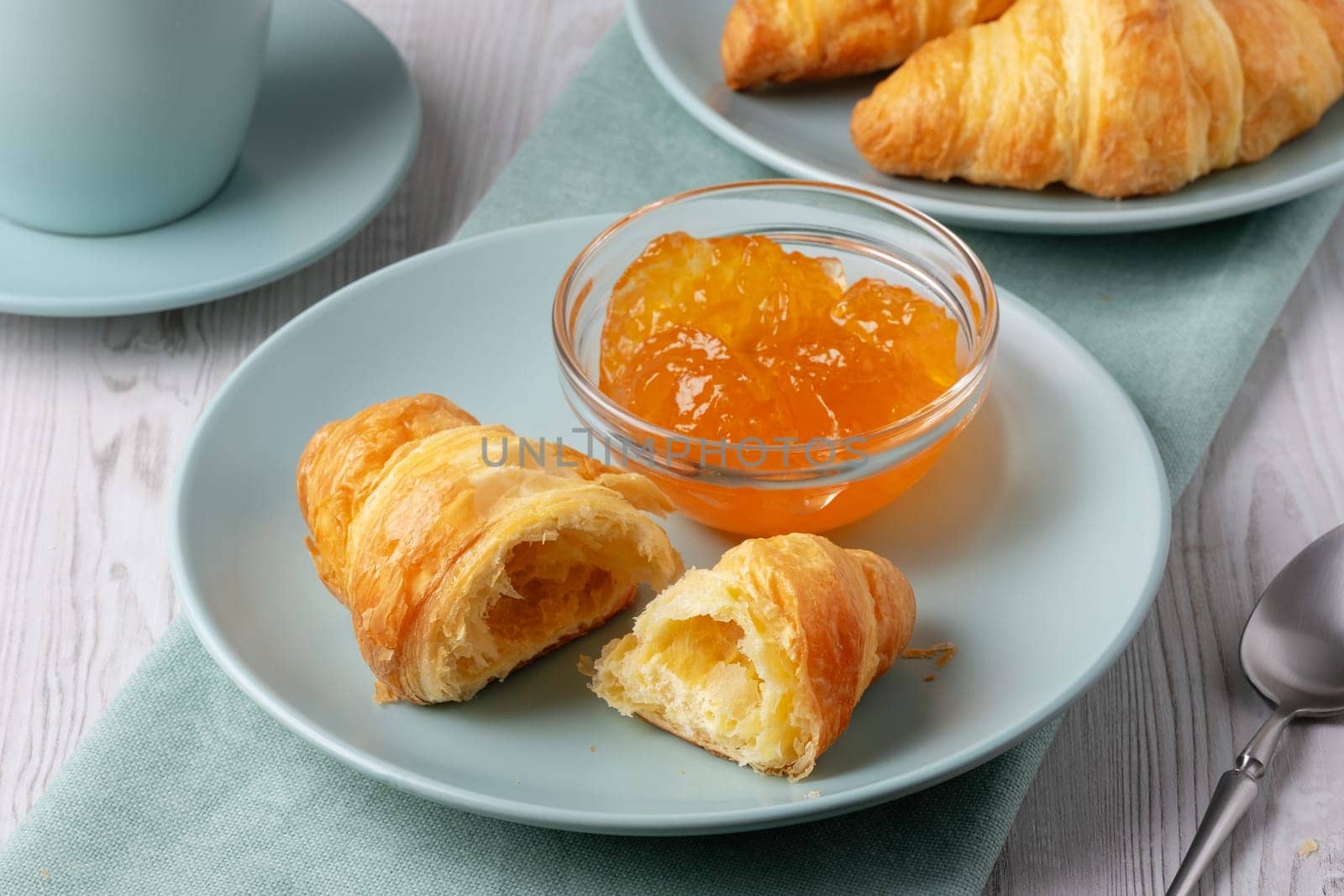 Freshly baked croissants served with jam and coffee on a light wooden table.