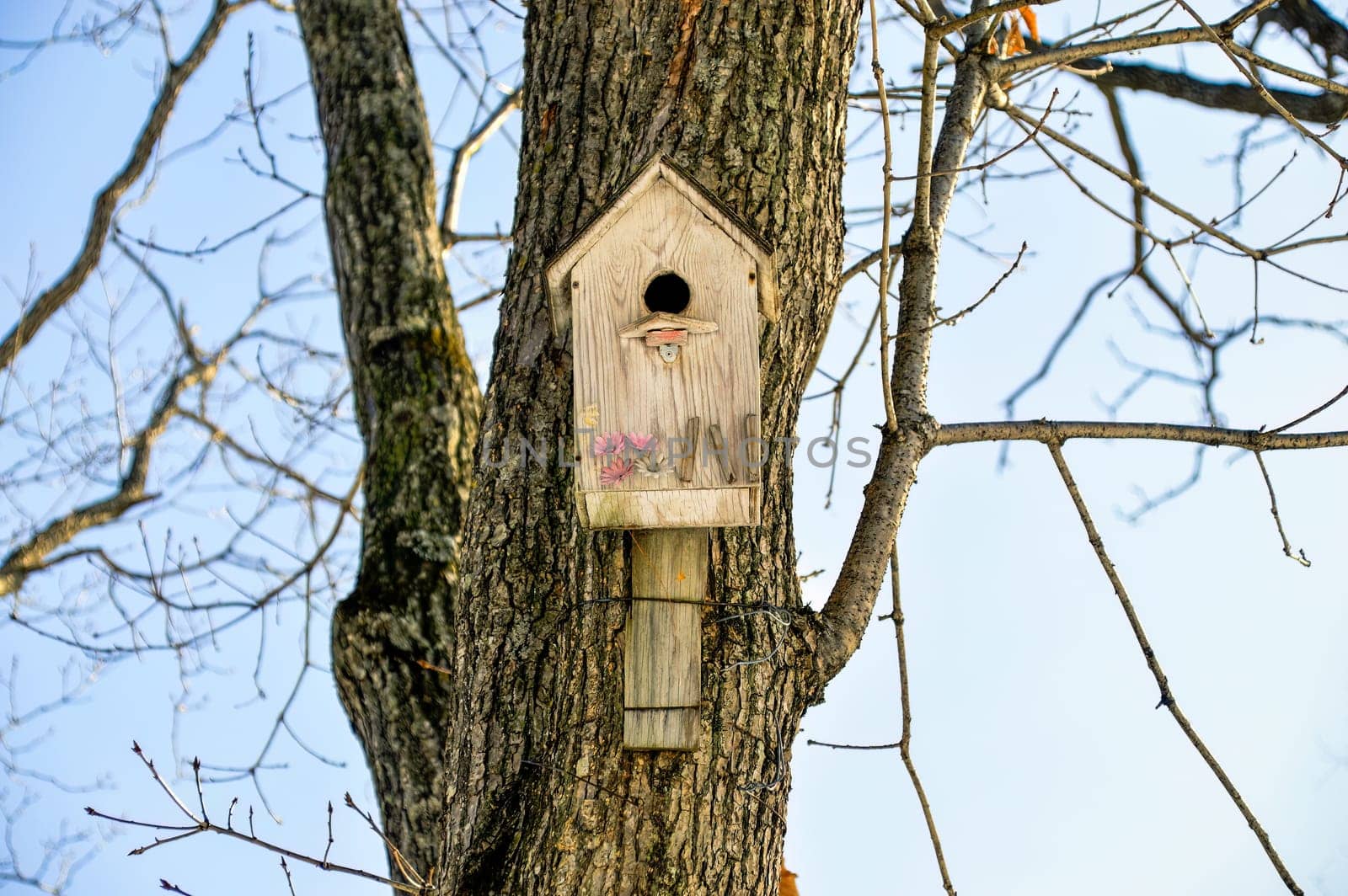 Wooden birdhouse with flowers. It hanging on the tree on sky background. Front view