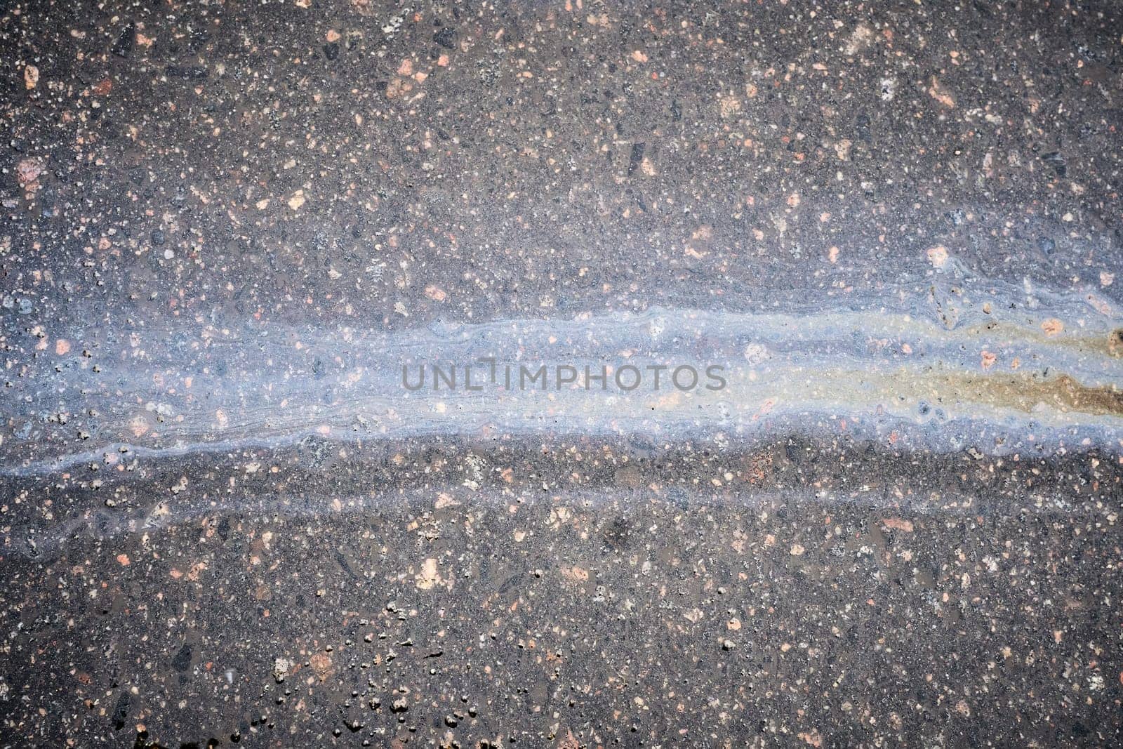 A vibrant oil slick stretches across the asphalt, reflecting various colors in the sunlight. This striking sight captures the interplay of light and pollution in the urban landscape
