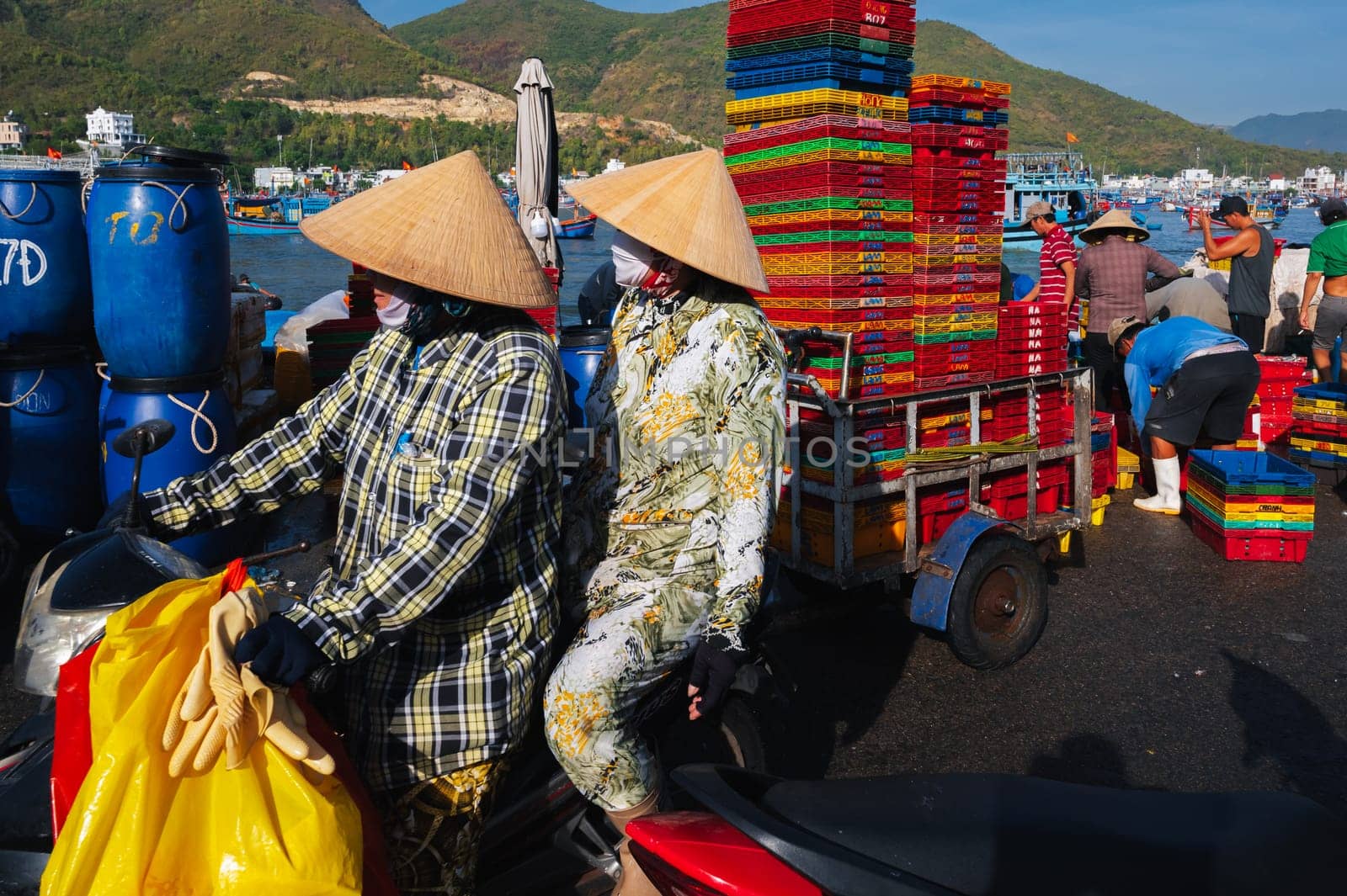 Vietnamese women ride on a tank through a fish market in a fishing harbor. Vietnam, Nha Trang - September 8, 2024