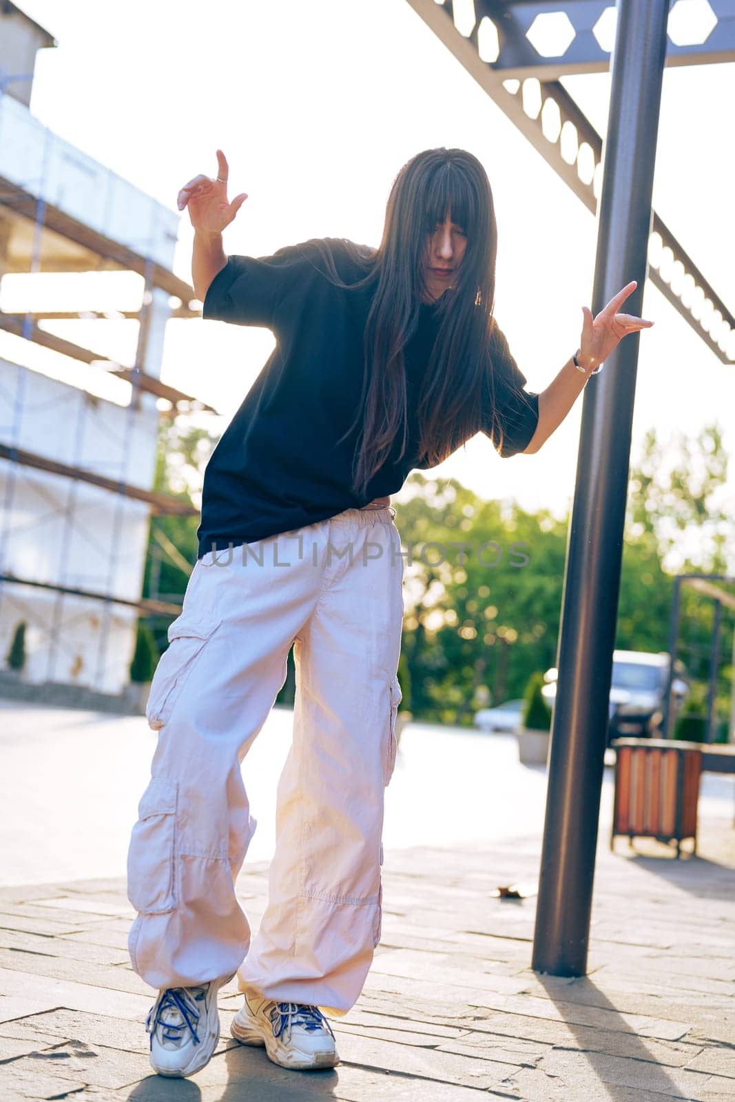 A dancer showcases an energetic routine in a sunlit urban area, wearing casual clothing and surrounded by construction. The warm light enhances the dynamic atmosphere.
