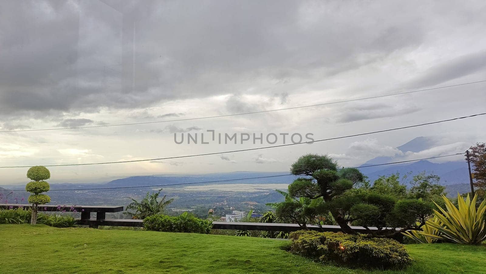 Serene hillside view featuring lush greenery, carefully shaped trees, distant mountains, and an overcast sky conveying tranquility in nature.