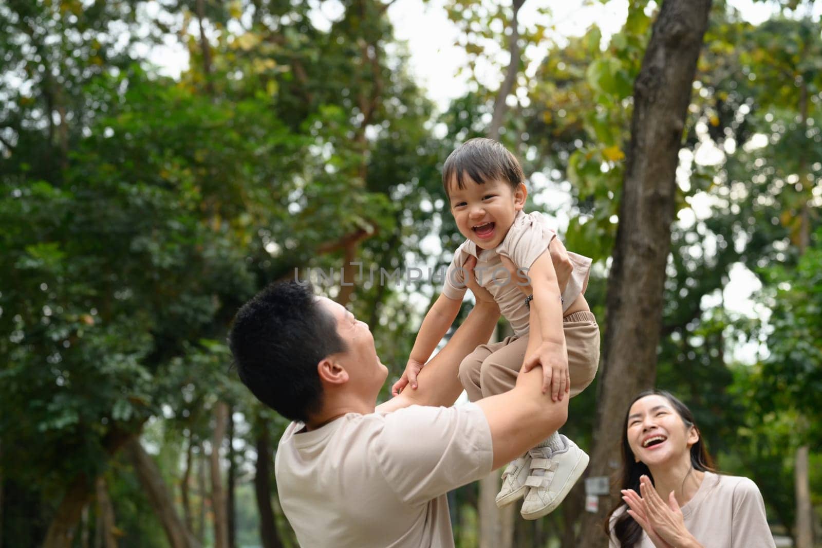 Happy father lifting his laughing son in the air. Outdoor leisure and family bonding concept.
