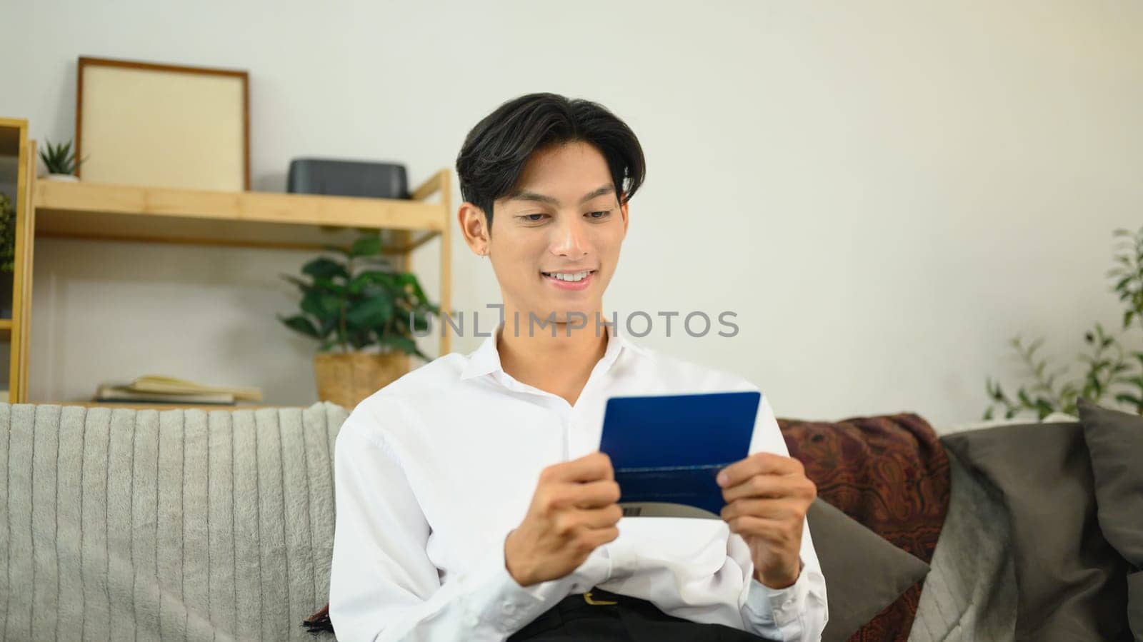 Young man sitting on a couch and reviewing his bankbook. Finance management concept.