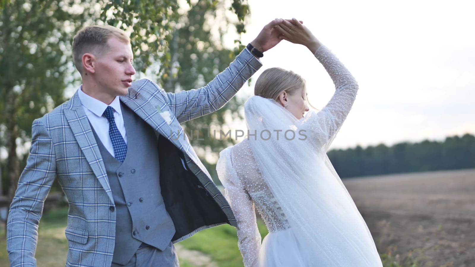 Happy couple dancing joyfully in a sunlit field, celebrating their wedding day together as the sun sets, creating a romantic atmosphere