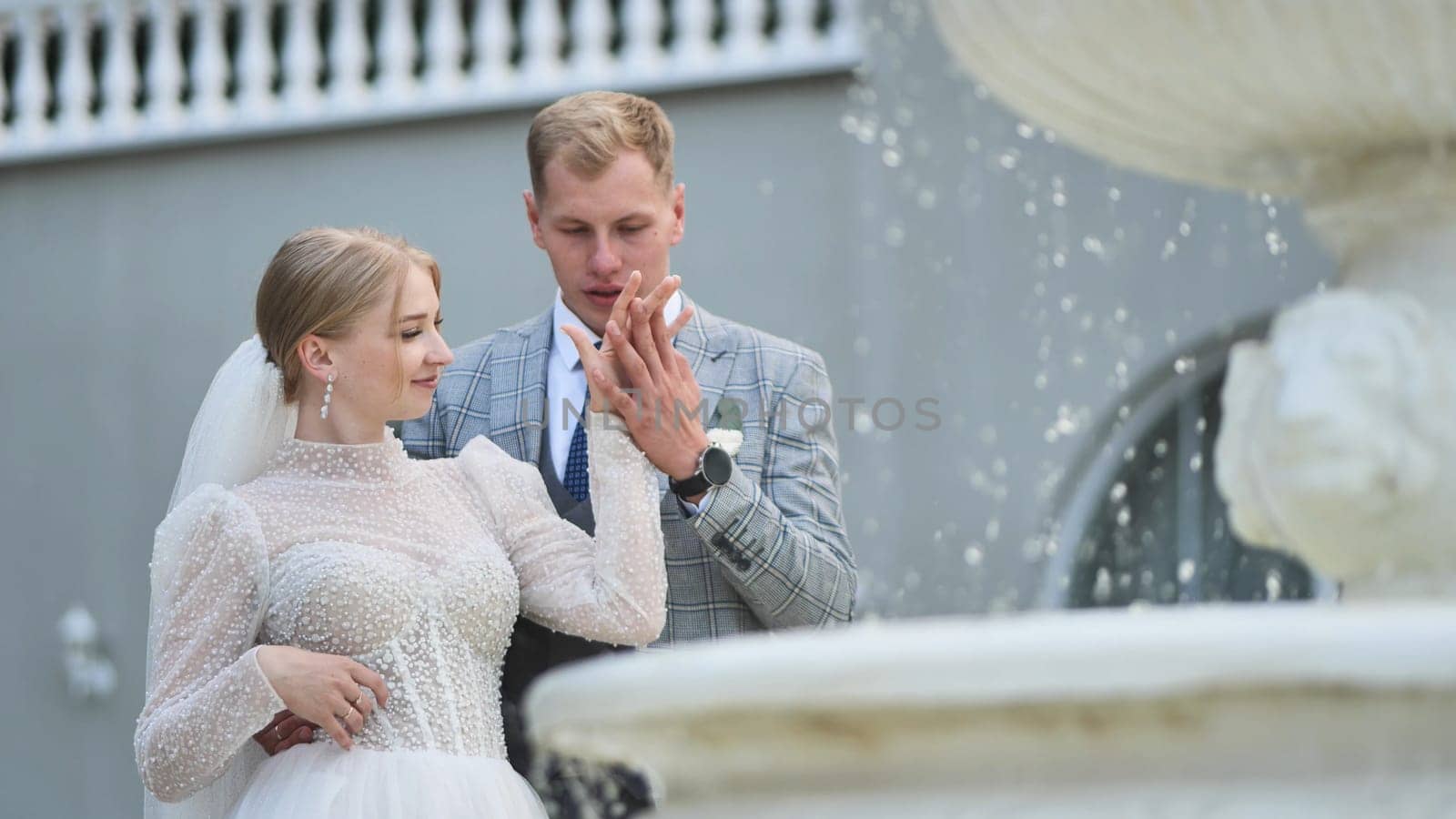 Newlywed couple holding hands beside elegant fountain, expressing romantic wedding day joy and intimate connection