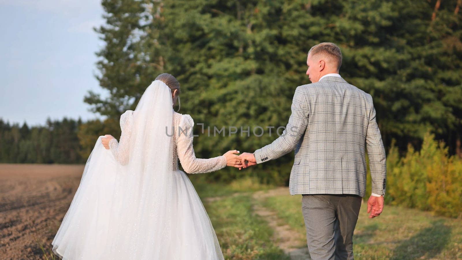 Newlywed couple holding hands walking down a path on their wedding day, celebrating their new life together