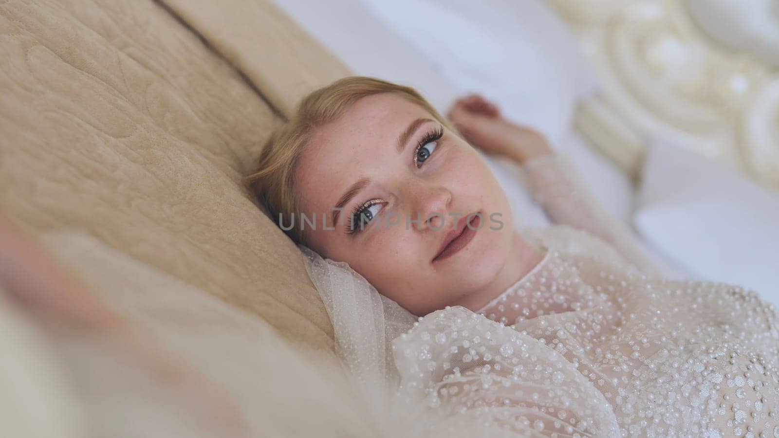Elegant bride resting on bed, wearing white wedding gown, experiencing serene moment before wedding ceremony, soft light highlighting delicate bridal preparation