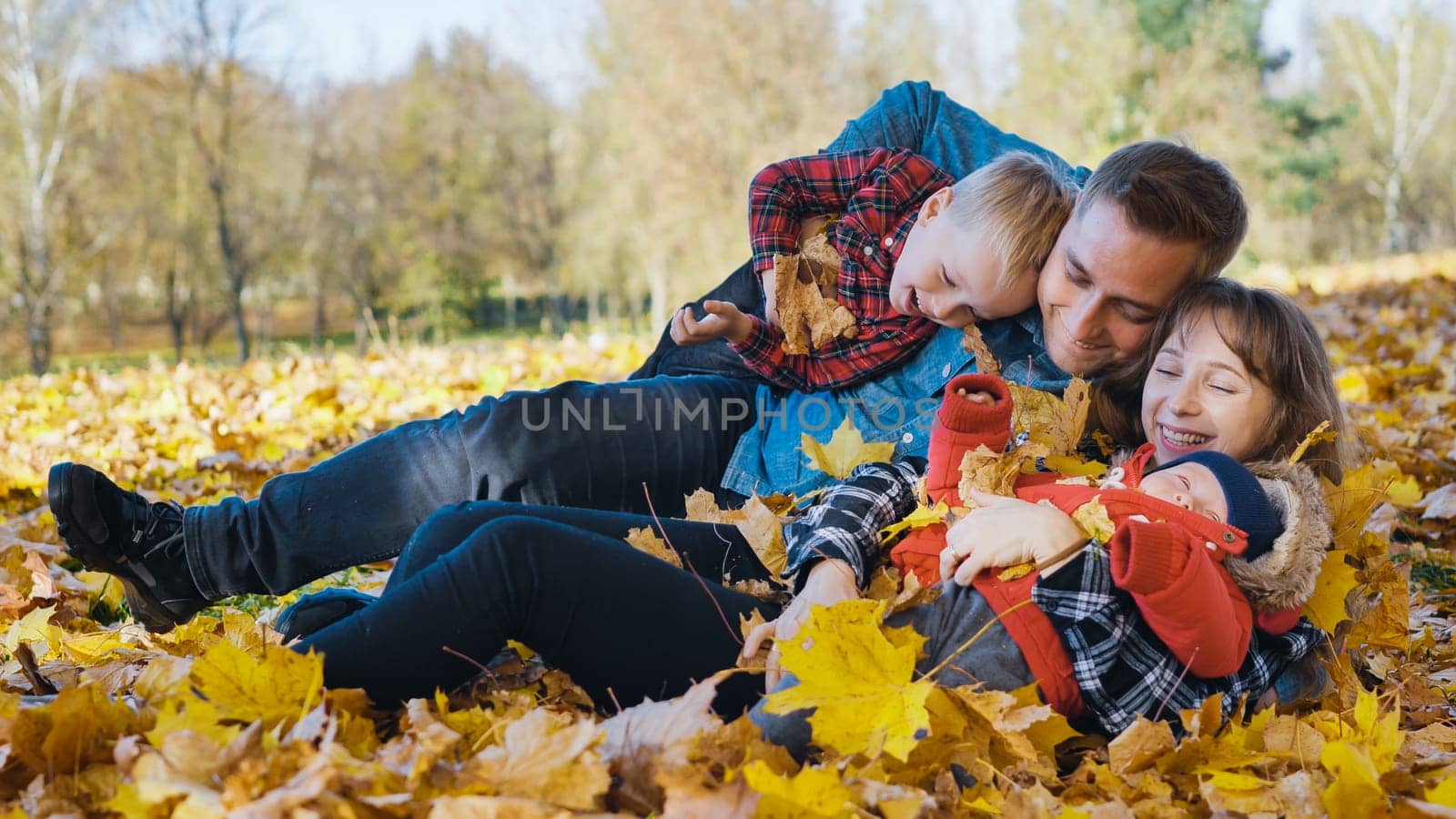 Happy family enjoying a sunny autumn day, playing joyfully with golden leaves in a vibrant park filled with colorful foliage