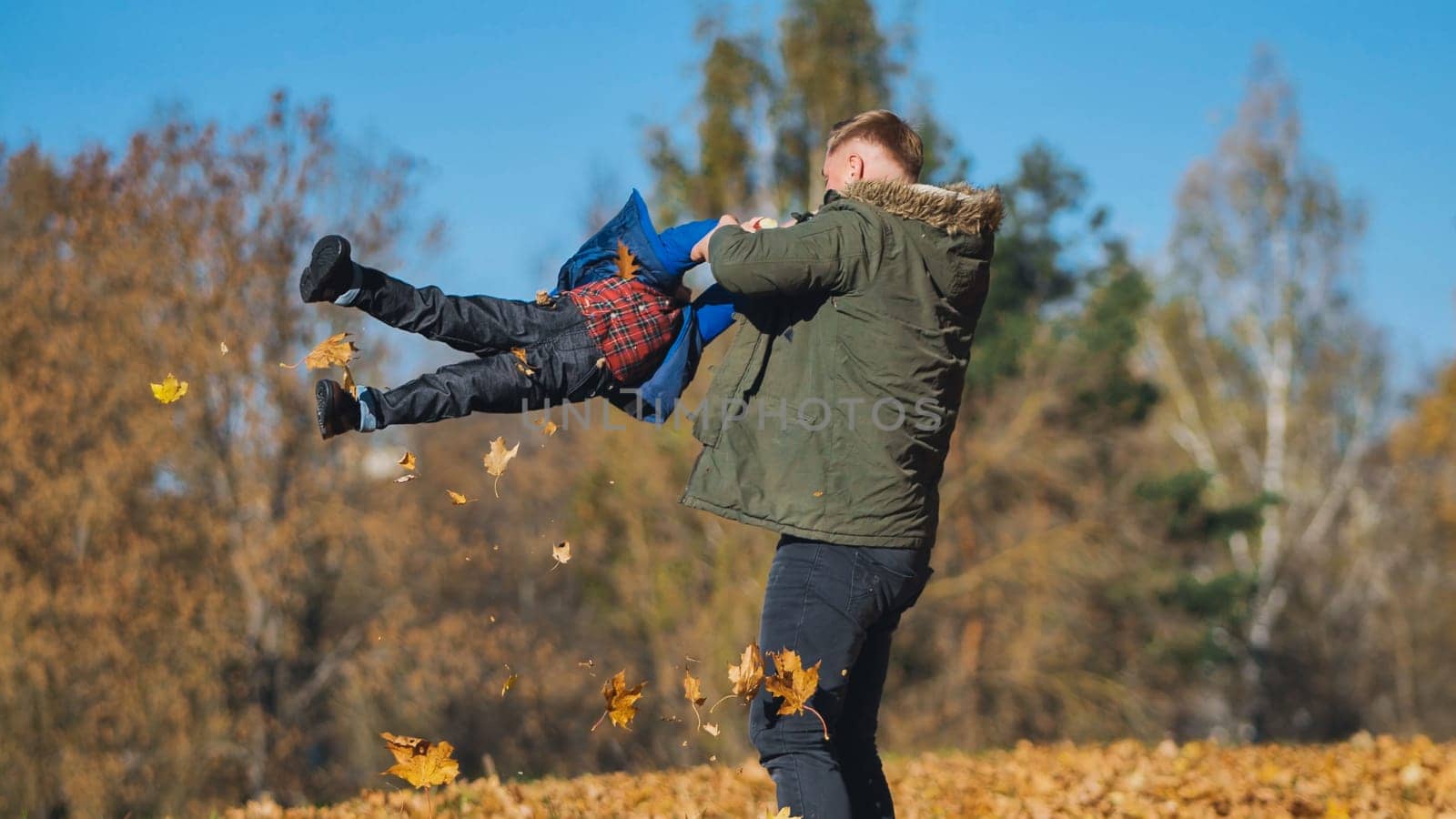 Father and son enjoying playful moments together in a vibrant park, surrounded by colorful autumn foliage on a sunny day