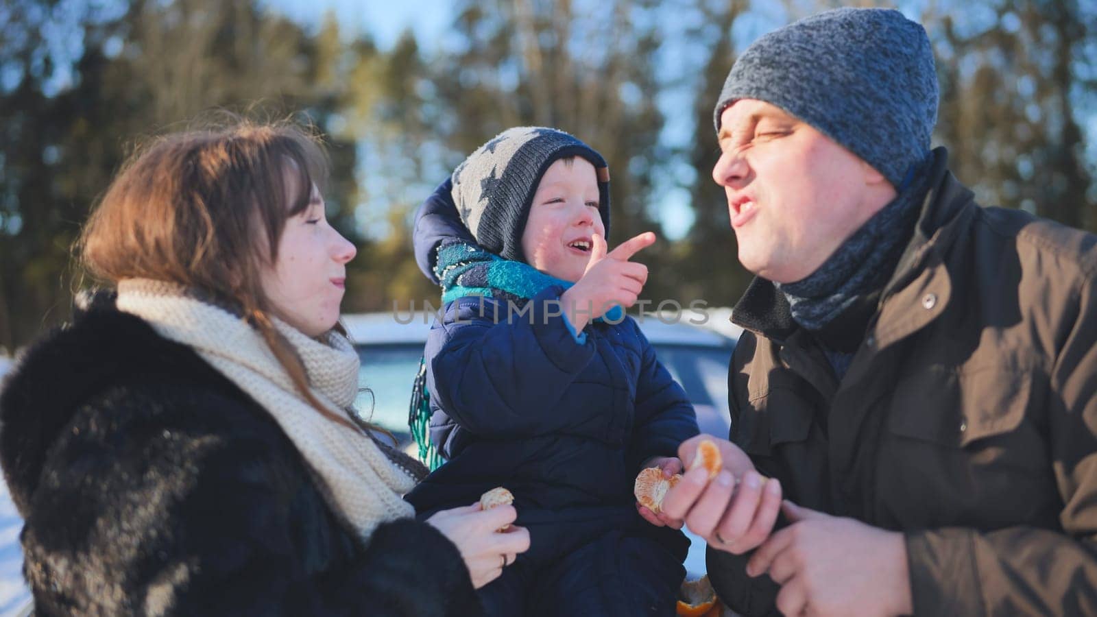 Happy family enjoying a bright winter day outdoors, laughing and sharing tangerines amidst the snowy landscape, creating joyful memories