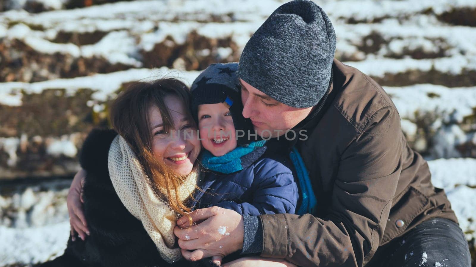 Happy family enjoying a winter day outdoors, embracing each other and sharing smiles while playing in the soft, glistening snow