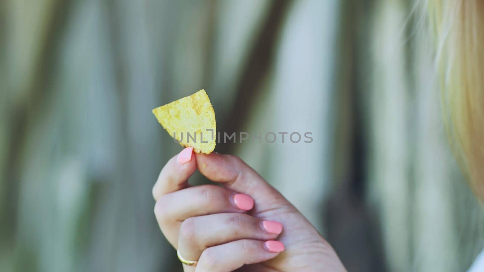 Woman with perfectly manicured nails holding a single golden potato chip, preparing for a deliciously crispy snack moment