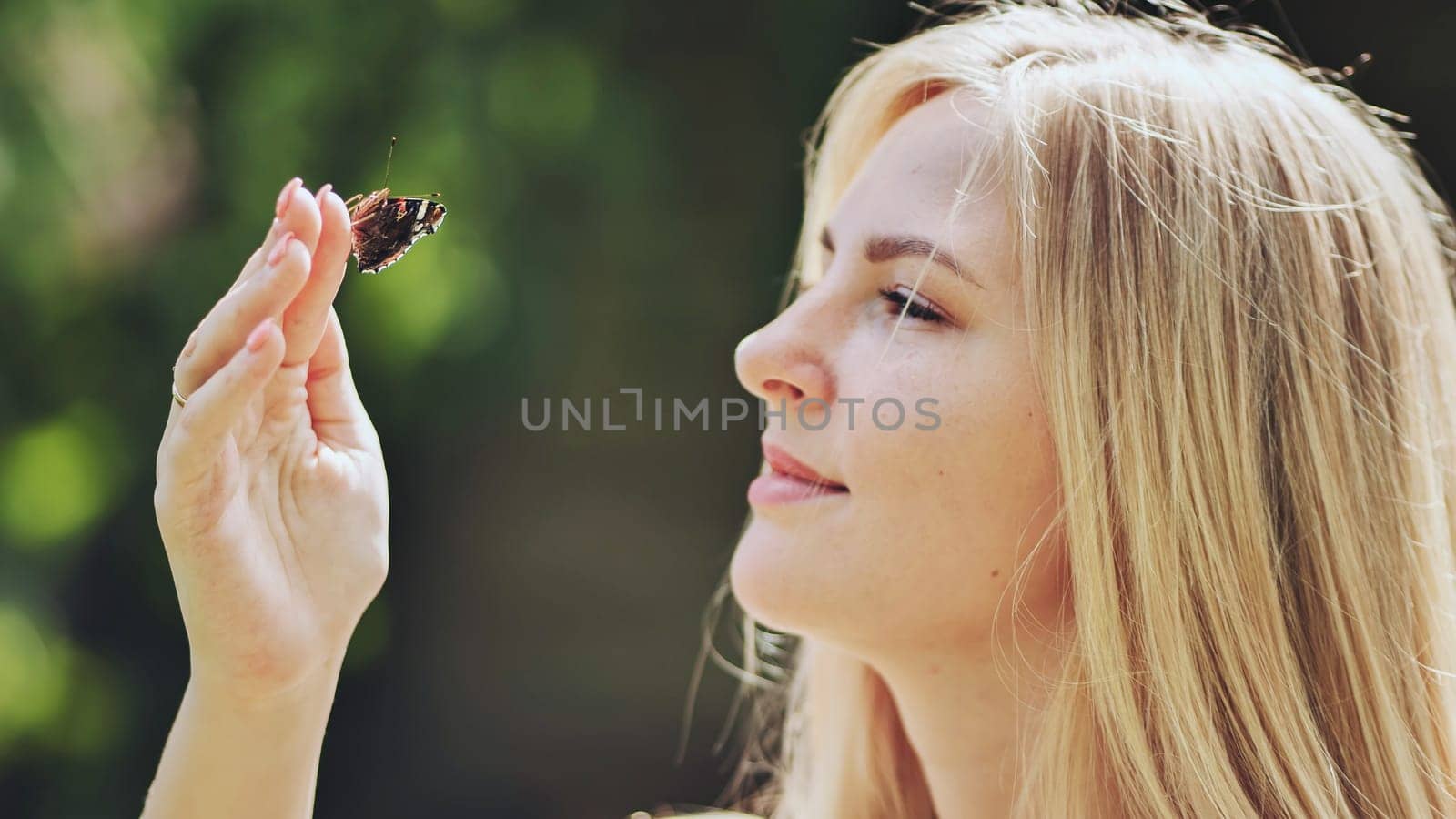 Young blonde woman holding a butterfly delicately on her finger, savoring the beauty of nature on a sunny summer day