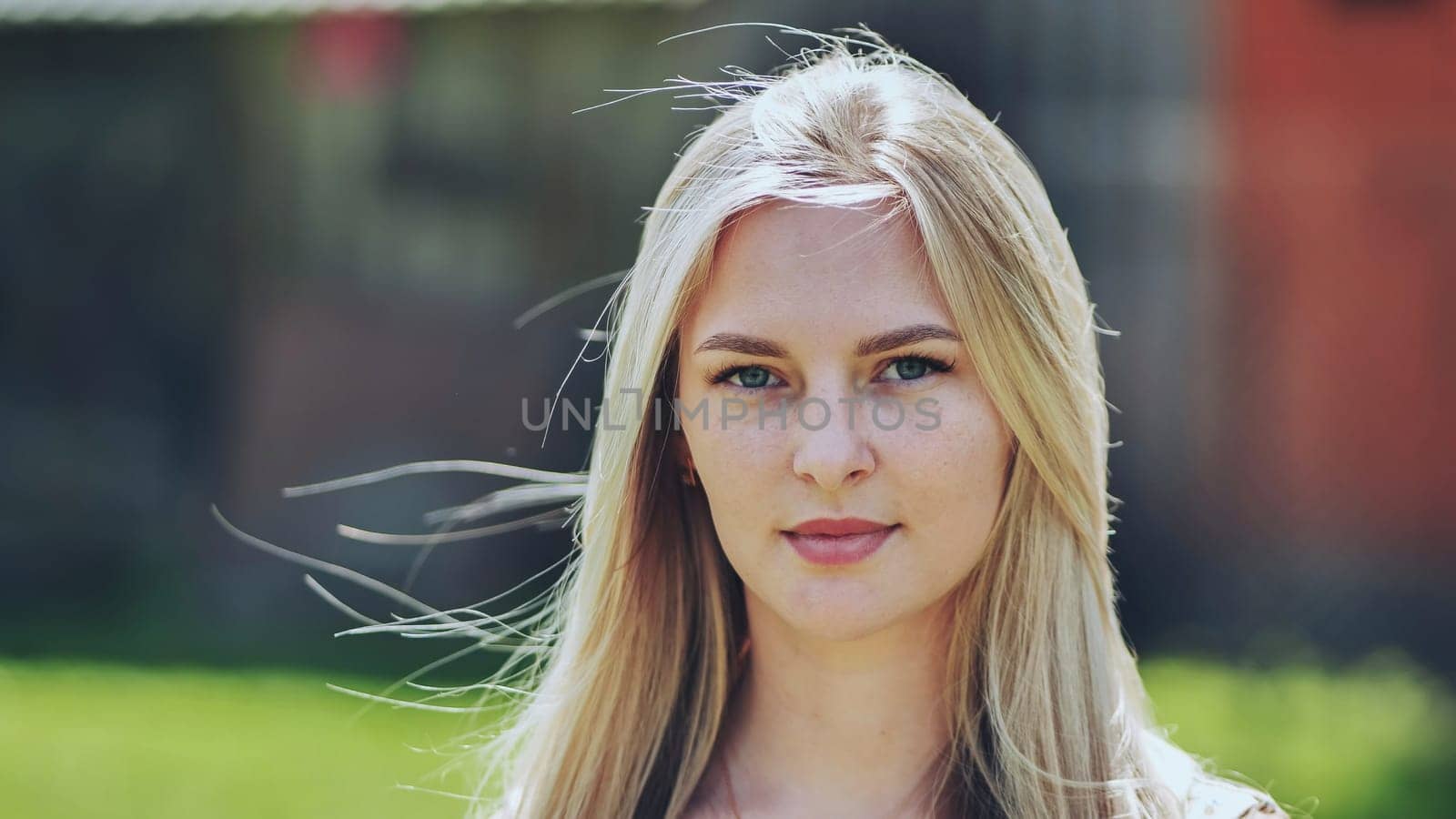 Blonde woman smiling, freckled skin glowing, hair windswept against natural outdoor background, radiating confidence