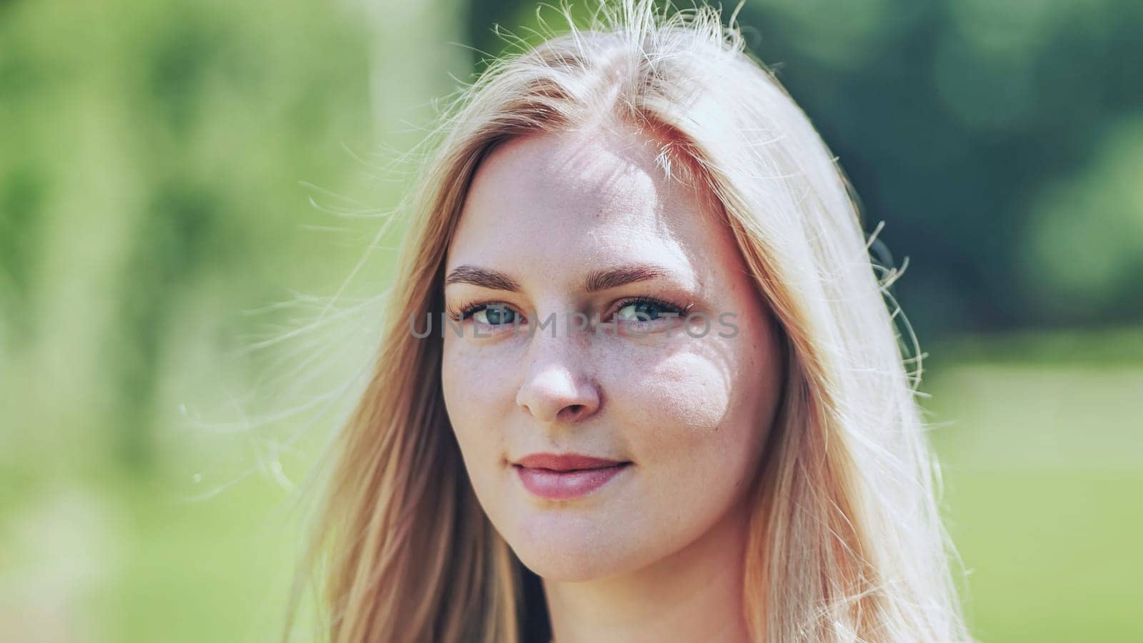 Portrait of a beautiful blonde woman with freckles smiling in a park during a sunny summer day