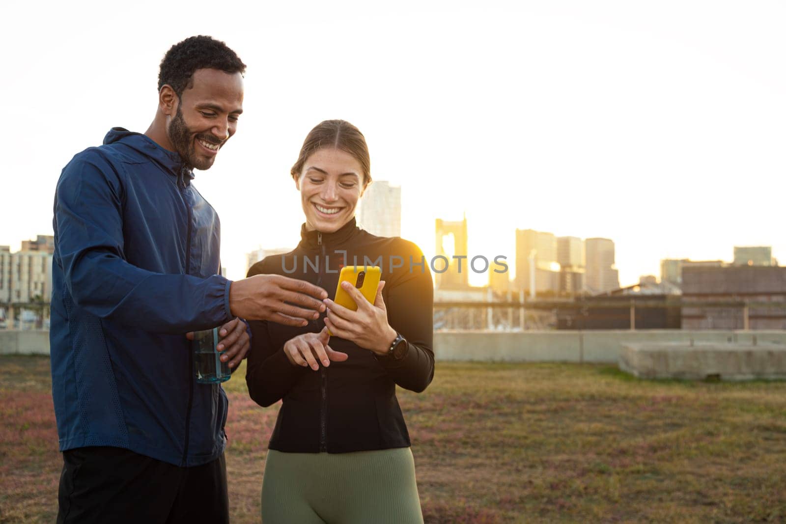 Two athletes checking their fitness app on a smartphone after training outdoors