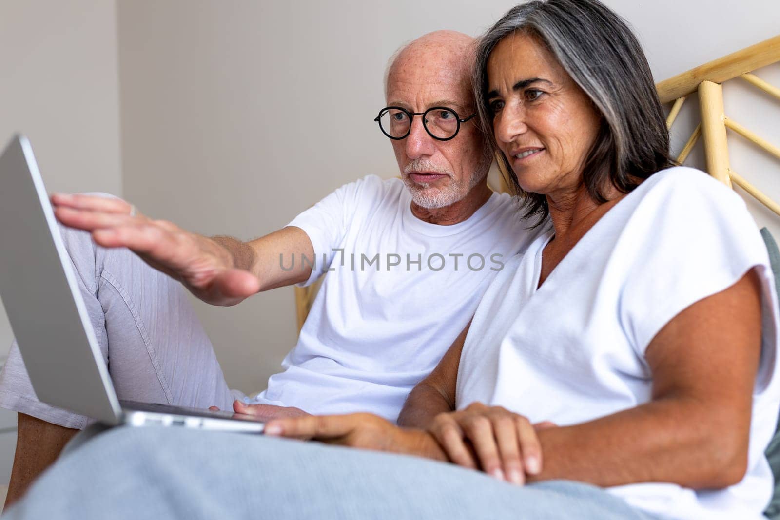 Mature heterosexual couple using laptop together in bed. Looking for information online. Lifestyle and technology concepts.