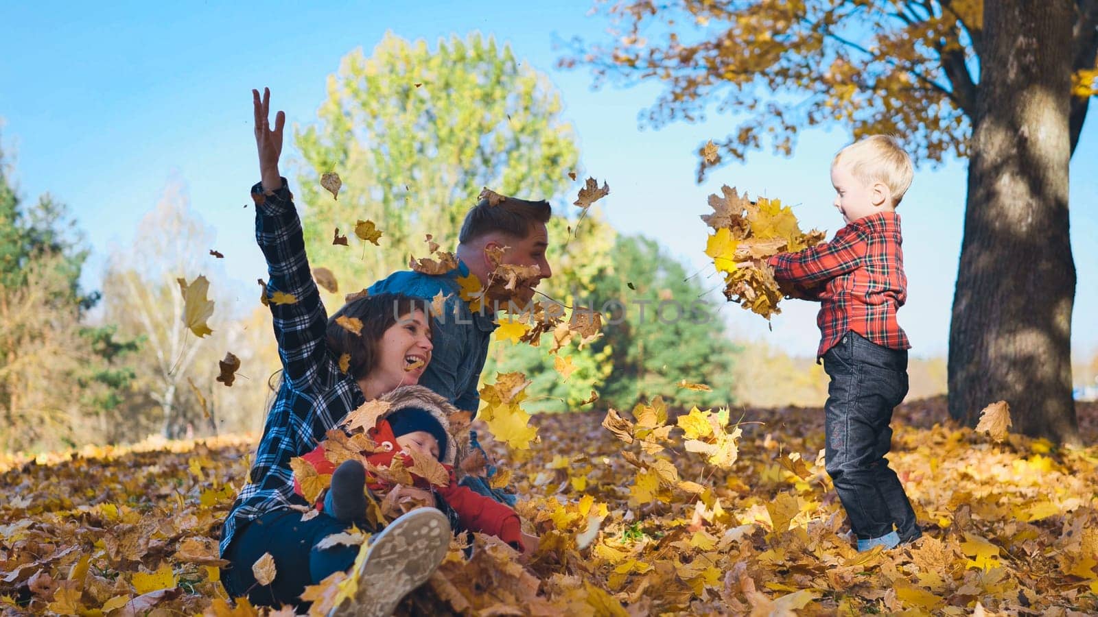 Cheerful parents and child tossing vibrant fallen leaves, playing outdoors during golden autumn afternoon