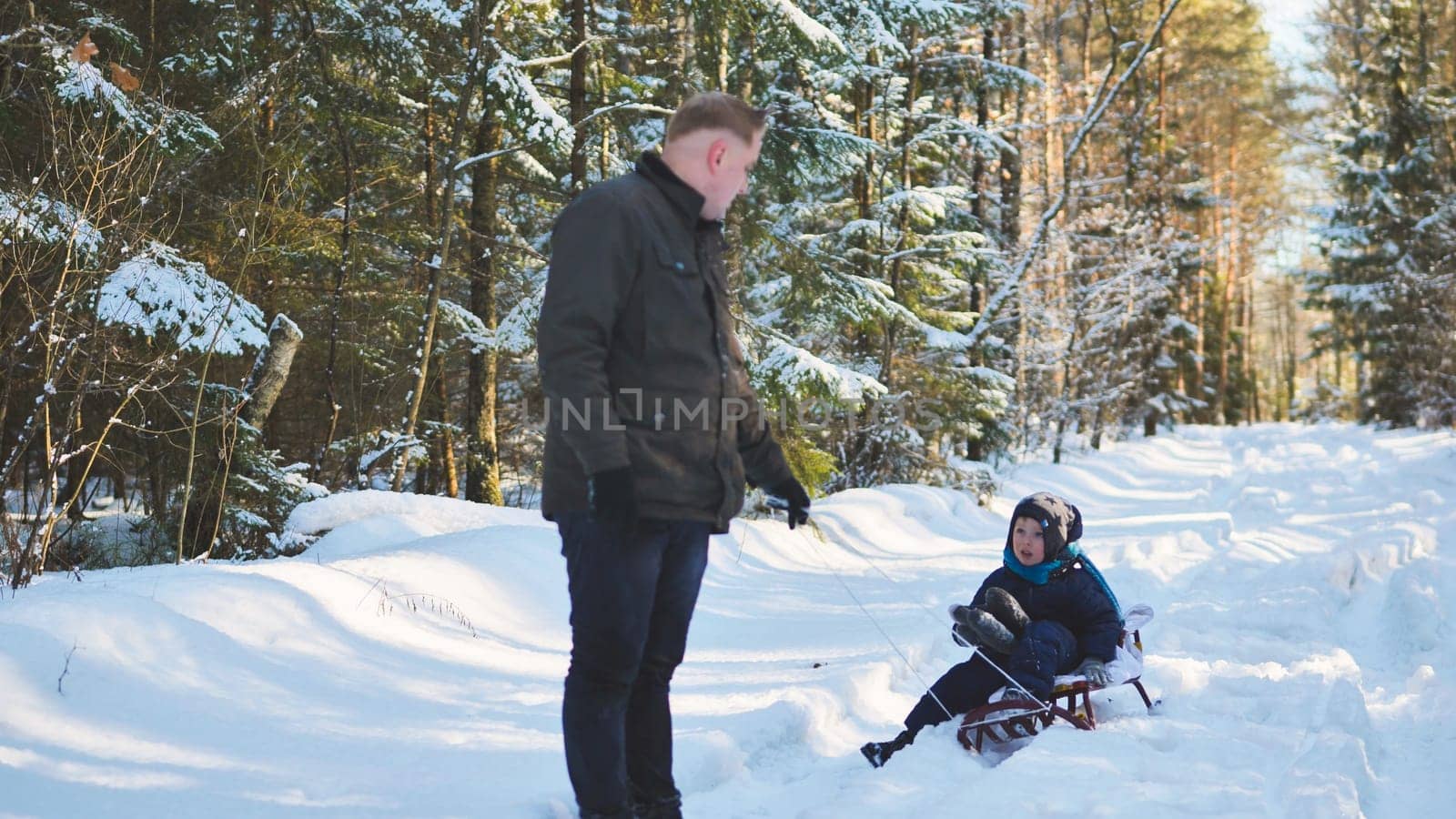 Dad pulling his son on a sled through snowy woods on a beautiful winter day, enjoying quality time together