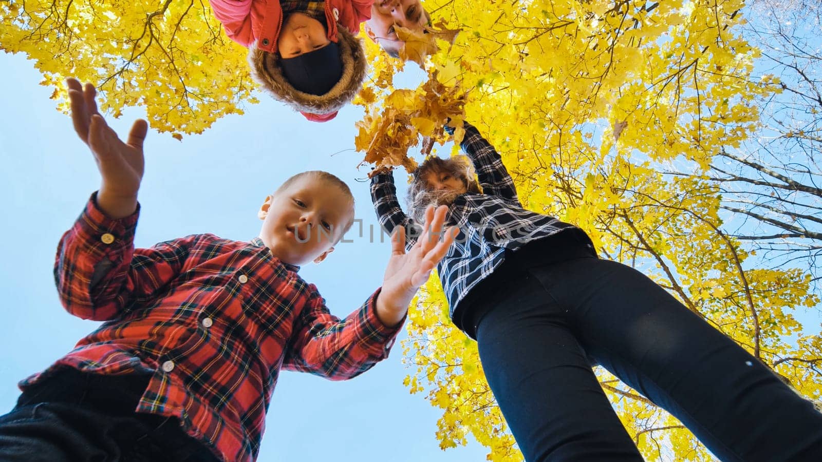 Happy family holding yellow maple leaves, playing together in autumn park, low angle view