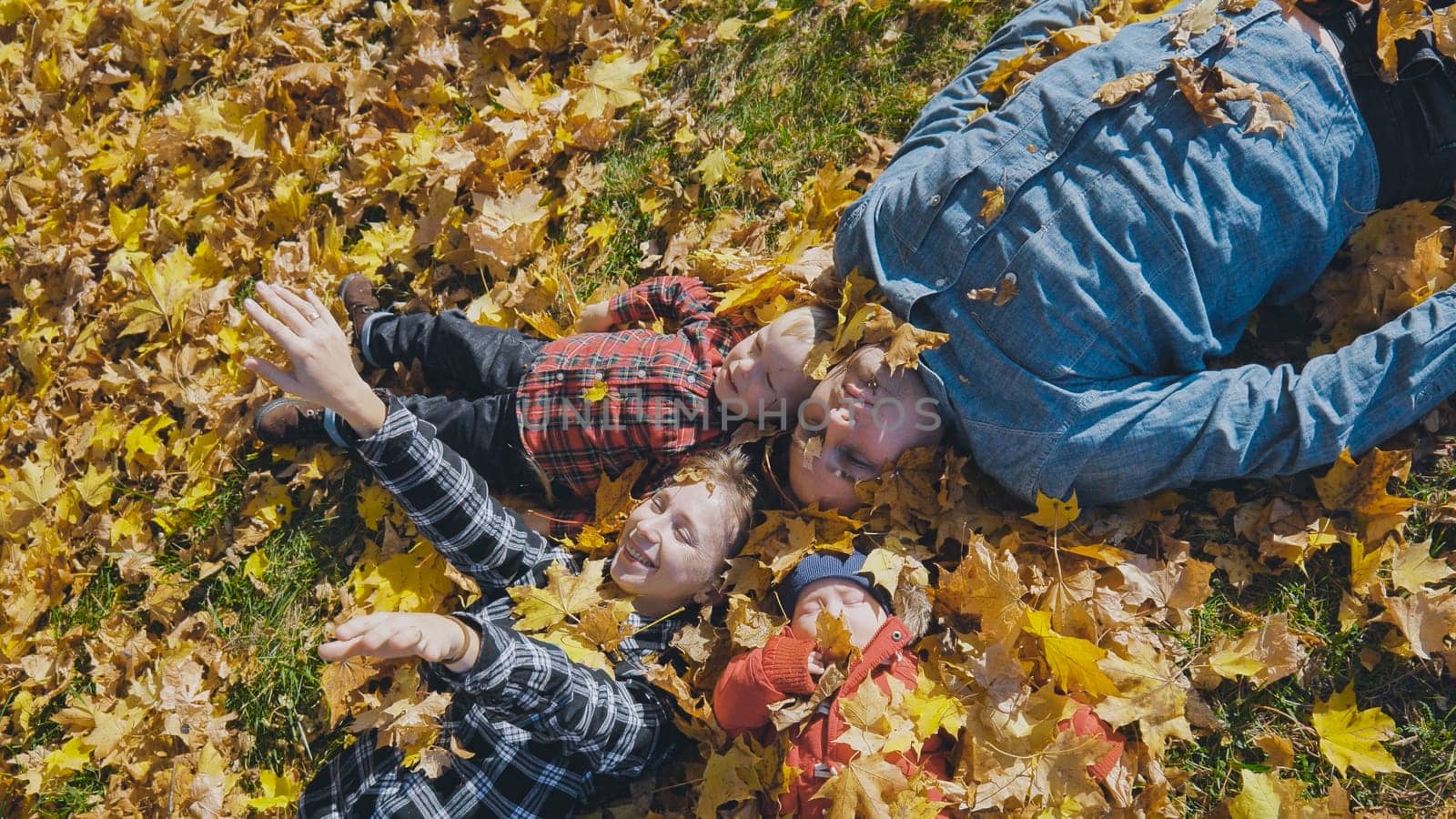Happy family enjoying a sunny autumn day lying down and playing in a park full of colorful leaves