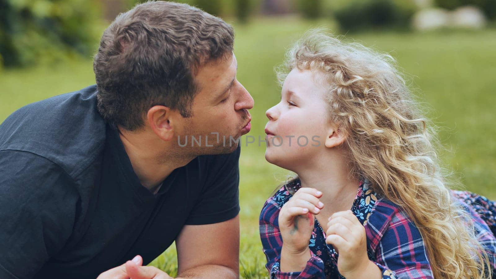 Father and daughter lying on grass are sending kisses to each other, enjoying a beautiful family day outdoors