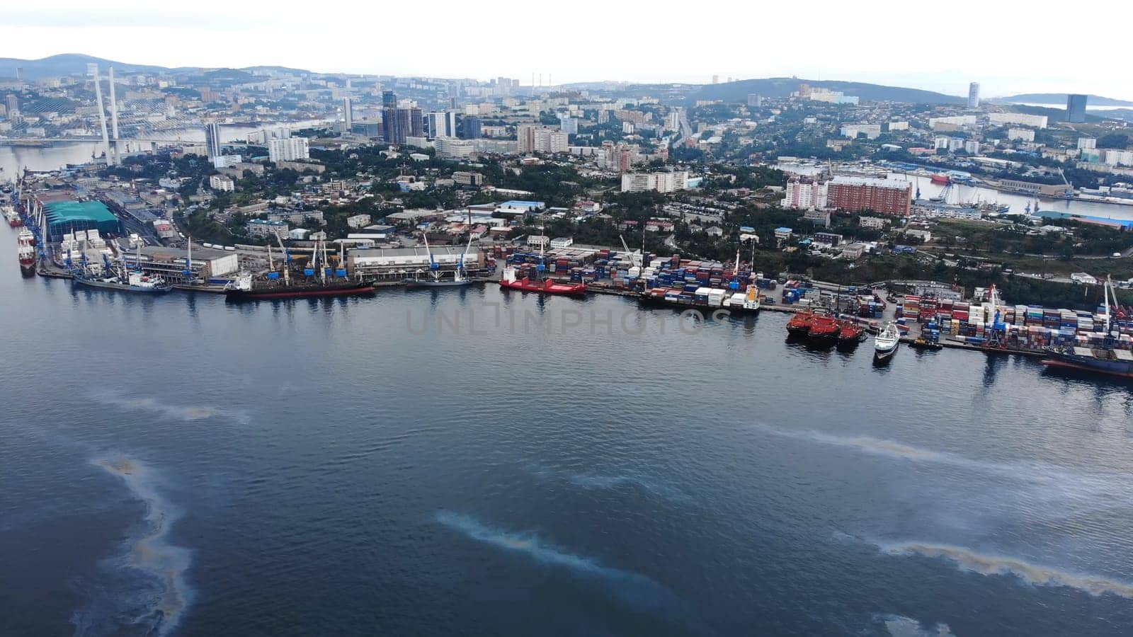 Oil spill spreading across marine surface near vladivostok port, revealing environmental damage from shipping vessels