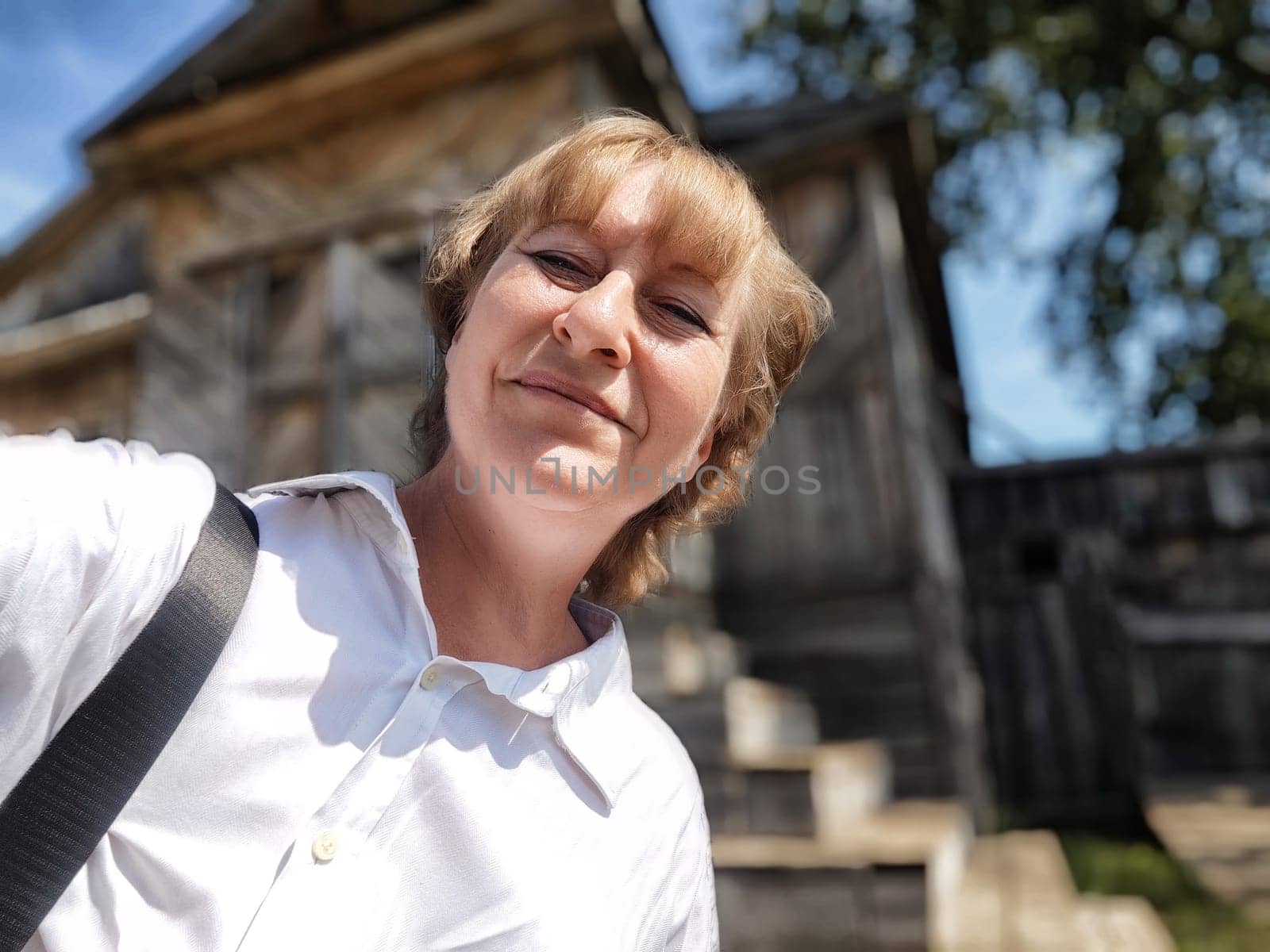 A mature blonde woman captures a cheerful selfie during her adventure trip, surrounded by scenic historic architecture.