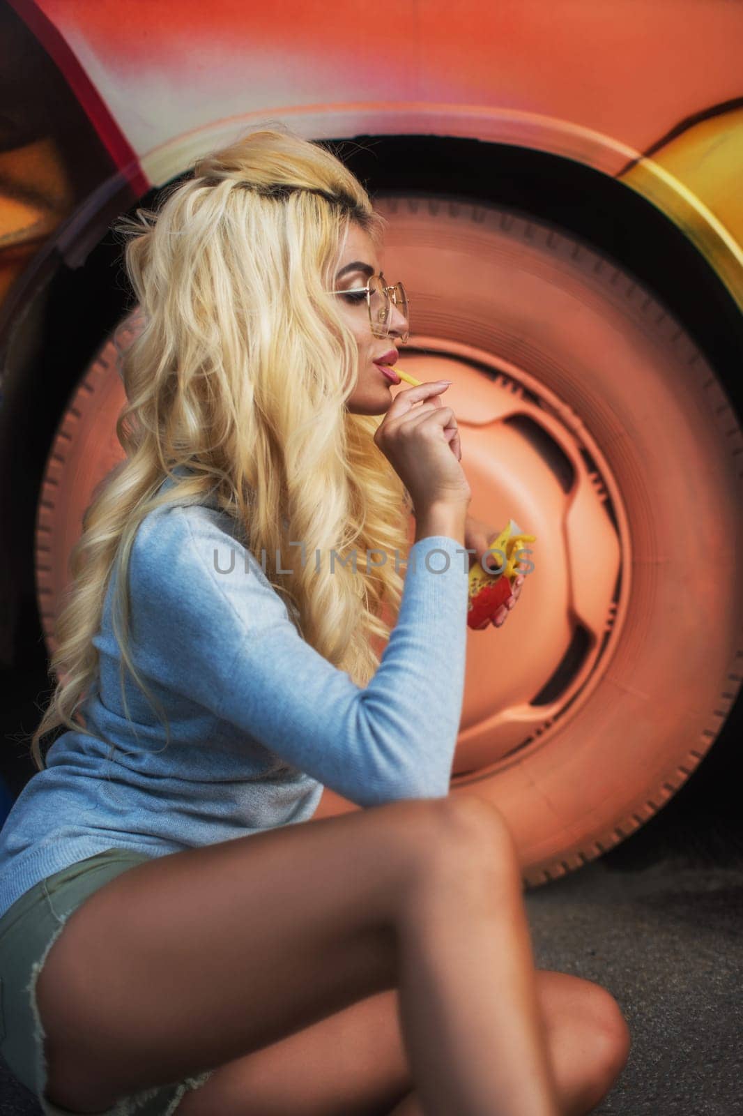 A fashionable young woman with blonde hair and glasses enjoys a snack while sitting