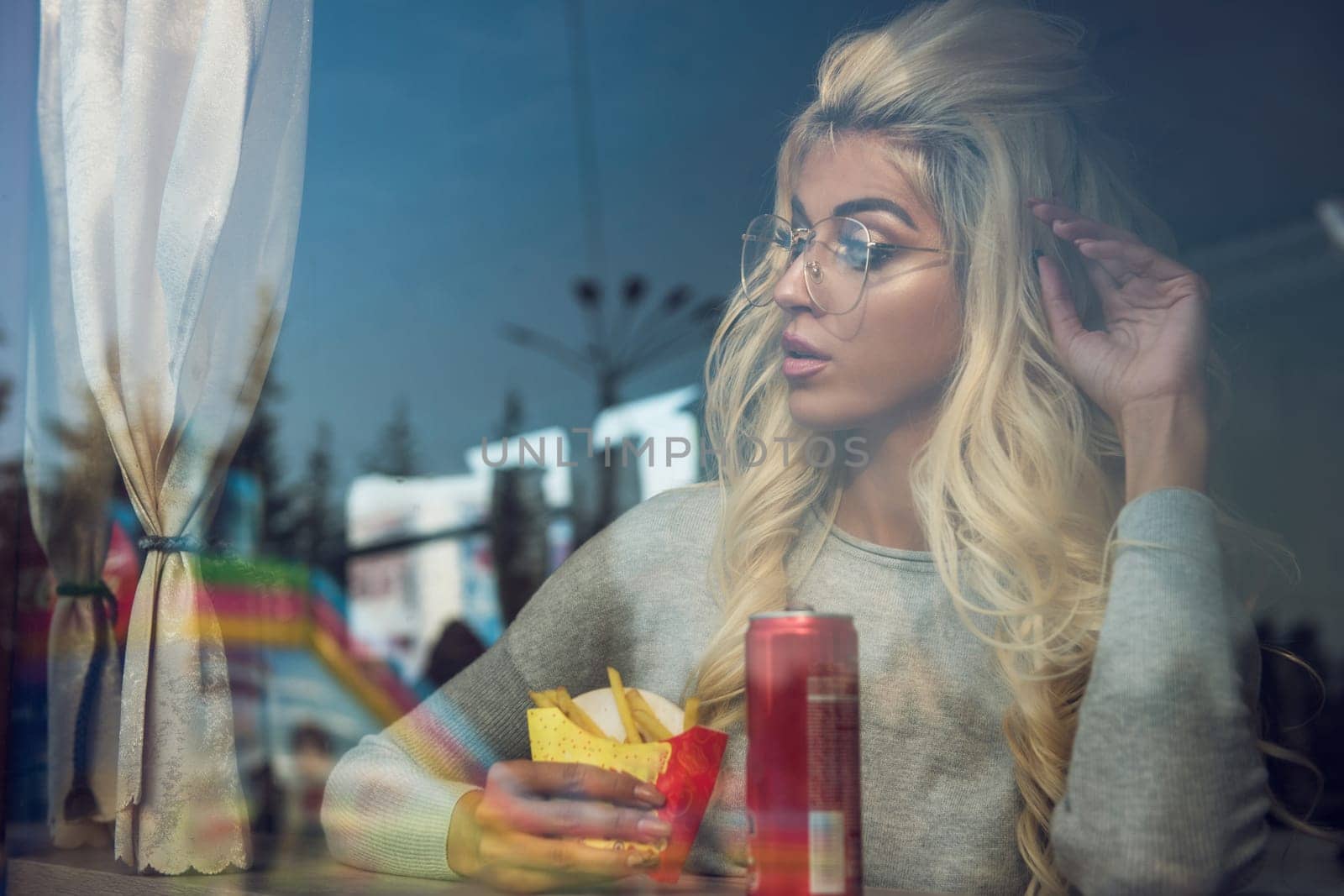 A fashionable young woman with blonde hair and glasses enjoys a snack