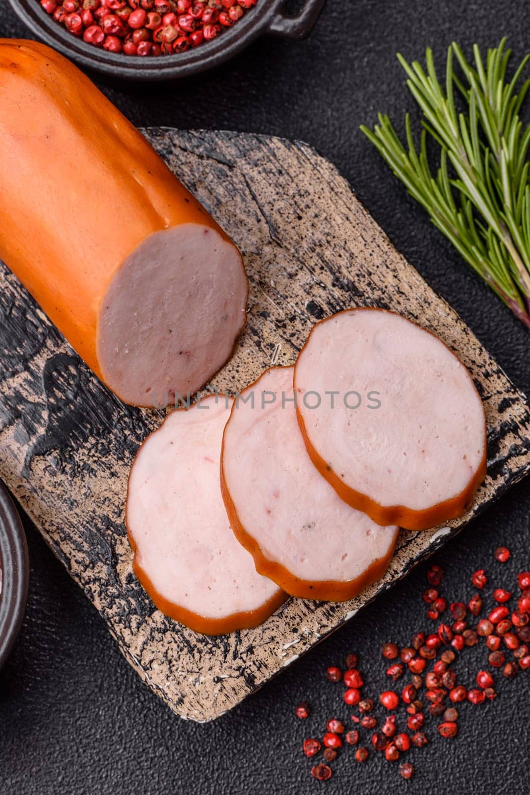 Delicious fresh ham cut into round slices with salt, spices and herbs on a dark concrete background