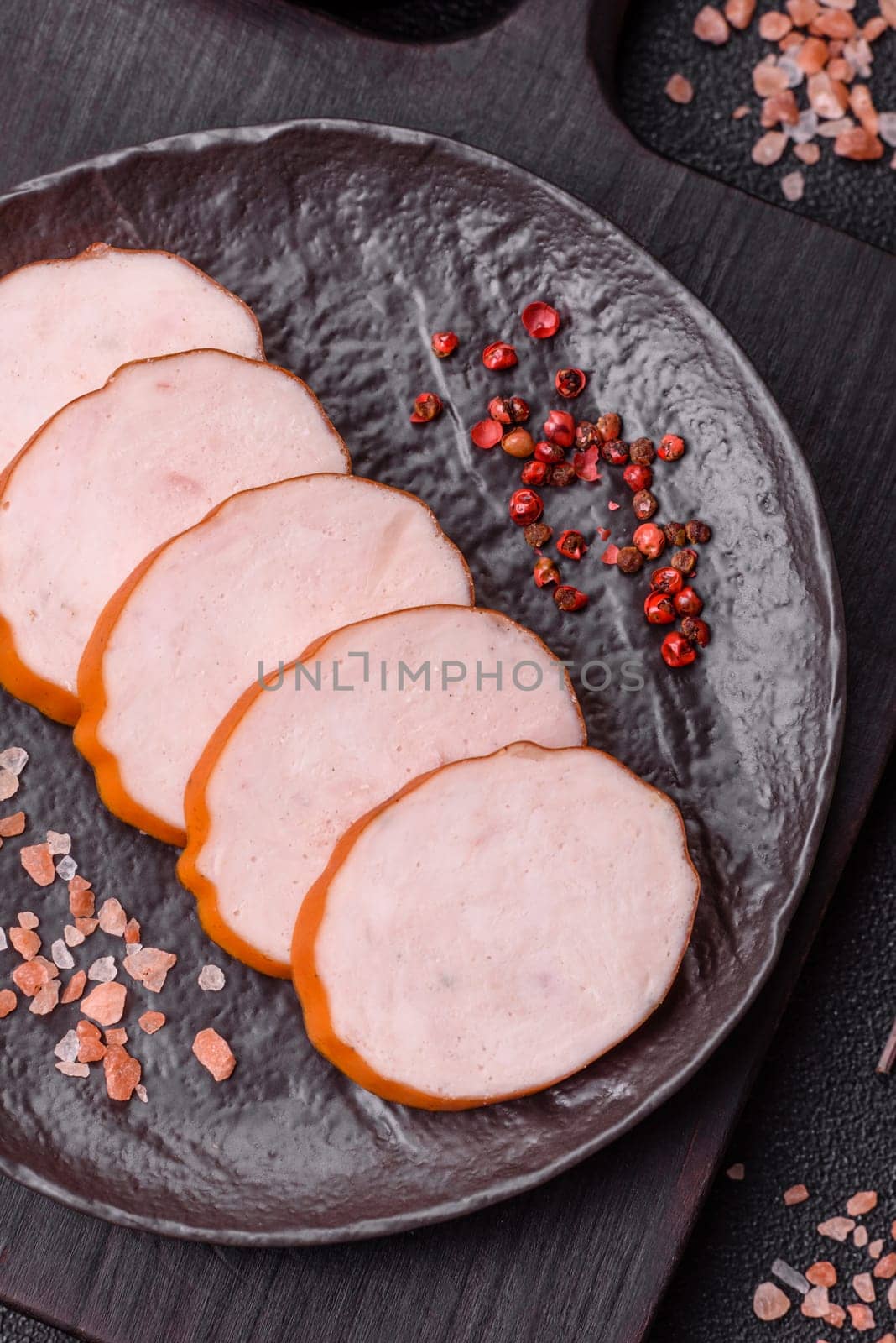 Delicious fresh ham cut into round slices with salt, spices and herbs on a dark concrete background