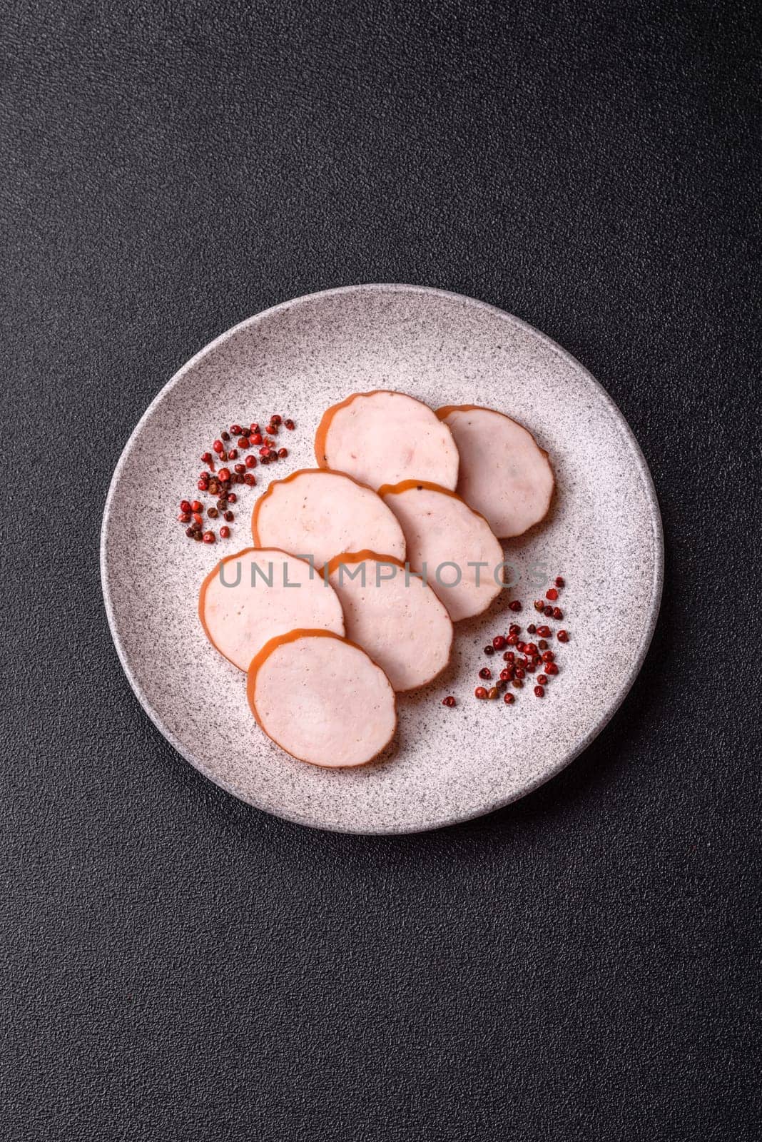 Delicious fresh ham cut into round slices with salt, spices and herbs on a dark concrete background