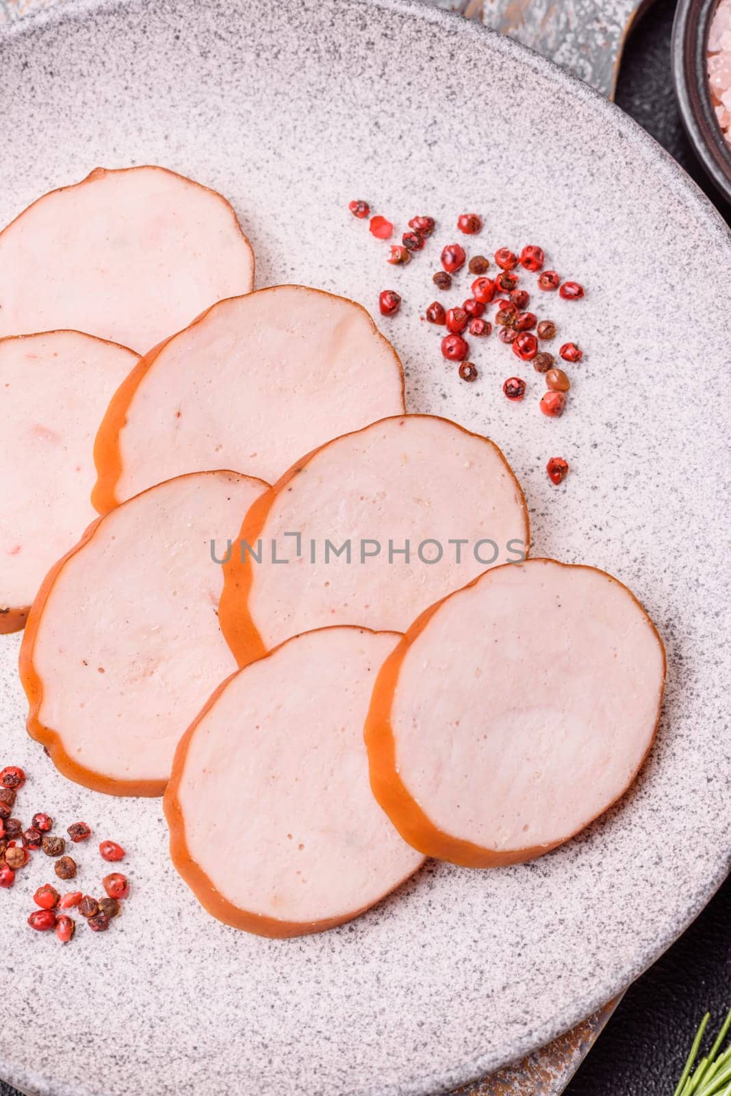 Delicious fresh ham cut into round slices with salt, spices and herbs on a dark concrete background