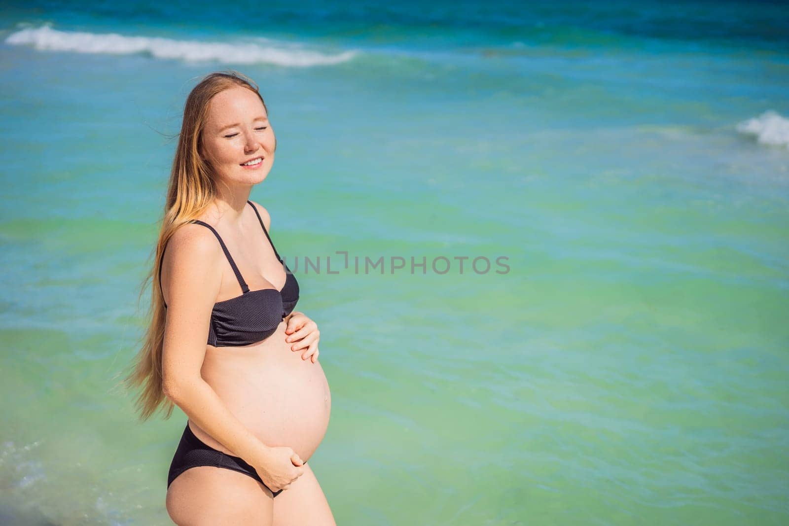 Radiant pregnant woman in a swimsuit, amid the stunning backdrop of a turquoise sea. Serene beauty of maternity by the shore.