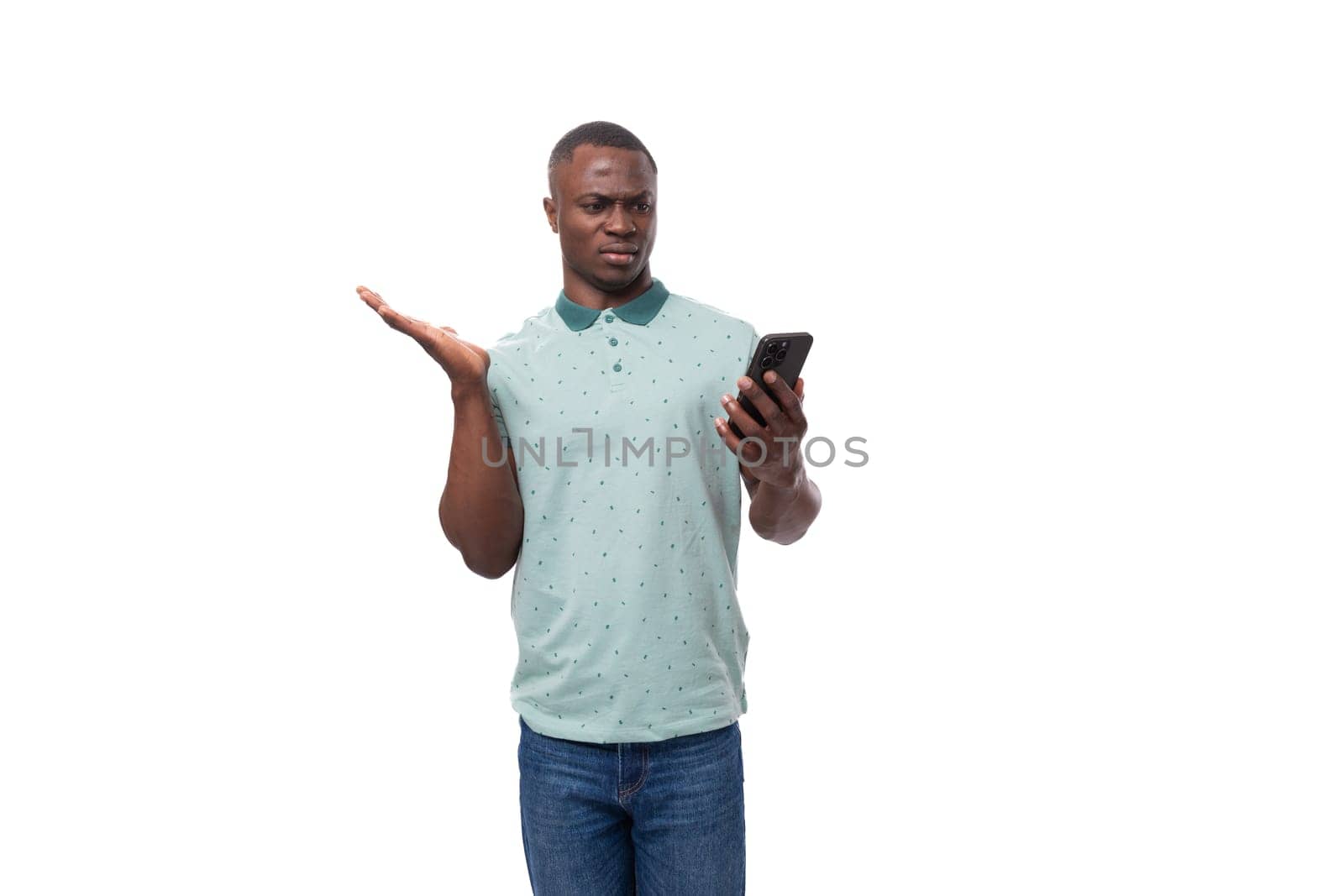 young smart american guy dressed in a mint t-shirt reads messages on a smartphone and is surprised.