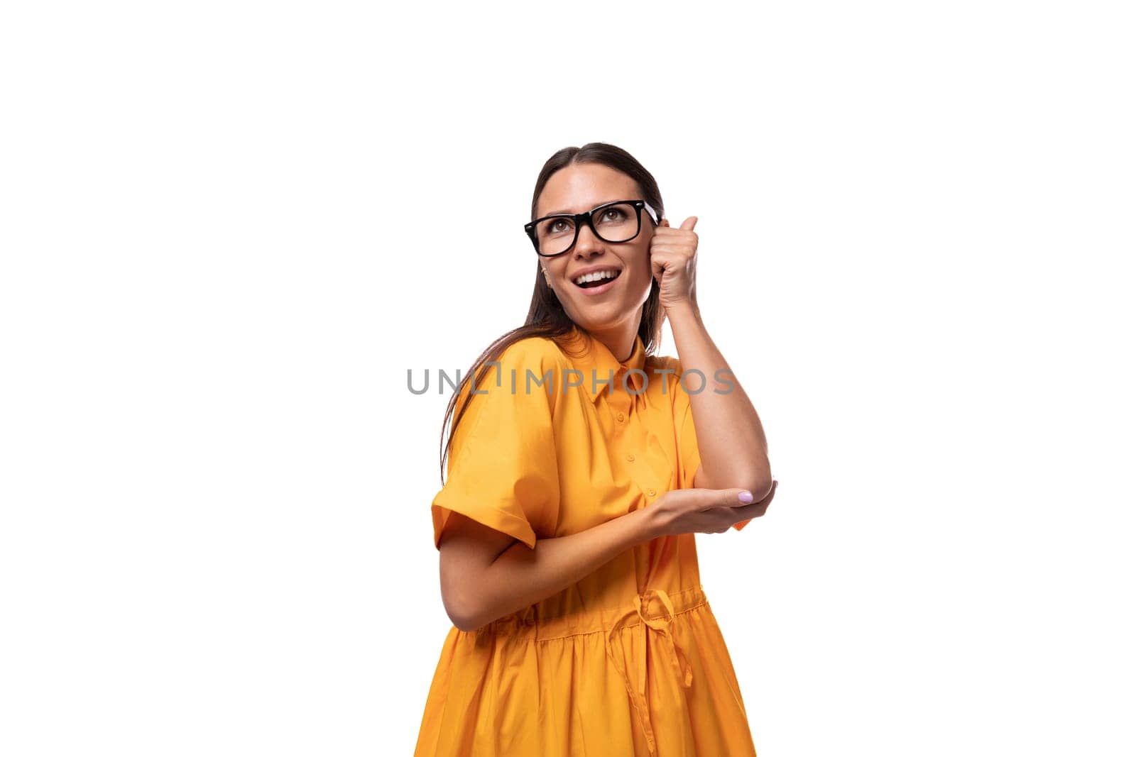 Caucasian young slender woman with black straight hair with glasses and in a yellow dress is flirting and shy.