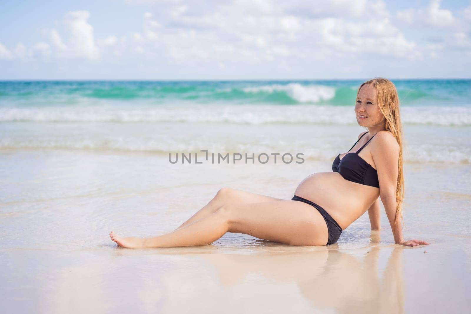 Radiant pregnant woman in a swimsuit, amid the stunning backdrop of a turquoise sea. Serene beauty of maternity by the shore.