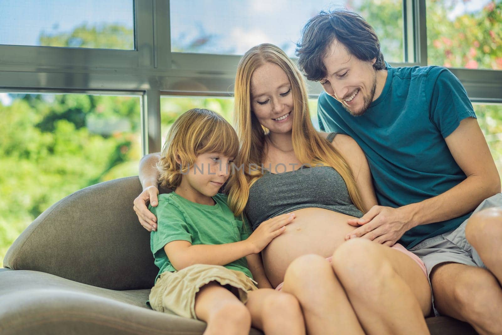 Expectant parents, mom, dad, and their eldest son share a heartwarming moment on the sofa, discussing the exciting journey of pregnancy by galitskaya