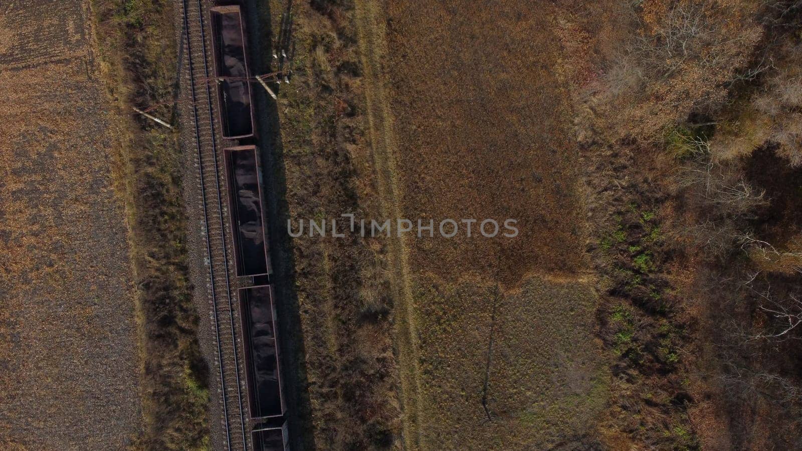 Aerial drone view flight over movement of train with carriages filled coal an autumn day. Top view Transportation and Rail freight. Freight cars or railway wagon rides on railroad. Delivery of cargo