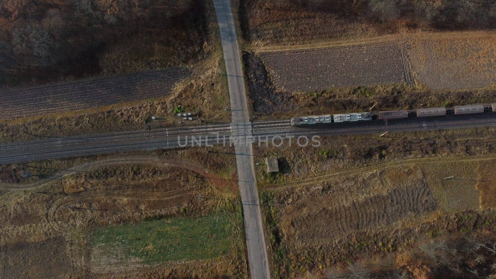 Top View Freight Train Passing Railway Crossing. Aerial Drone View Flight Over Intersection of Railway Tracks and Asphalt Road. Transportation, Rail freight, Delivery. Railway Wagon Rides on Railroad.