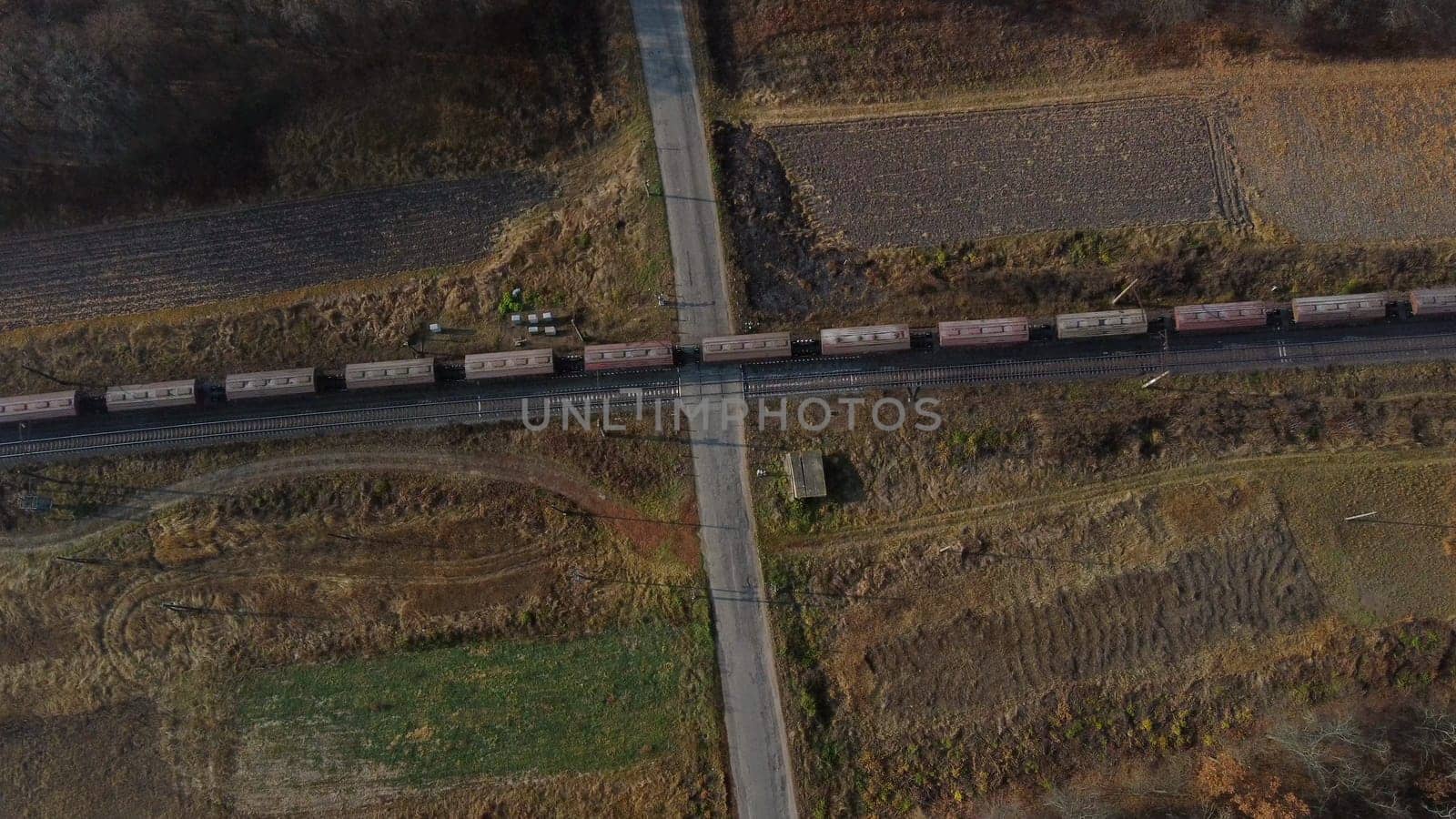 Top View Freight Train Passing Railway Crossing. Aerial Drone View Flight Over Intersection of Railway Tracks and Asphalt Road. Transportation, Rail freight, Delivery. Railway Wagon Rides on Railroad.