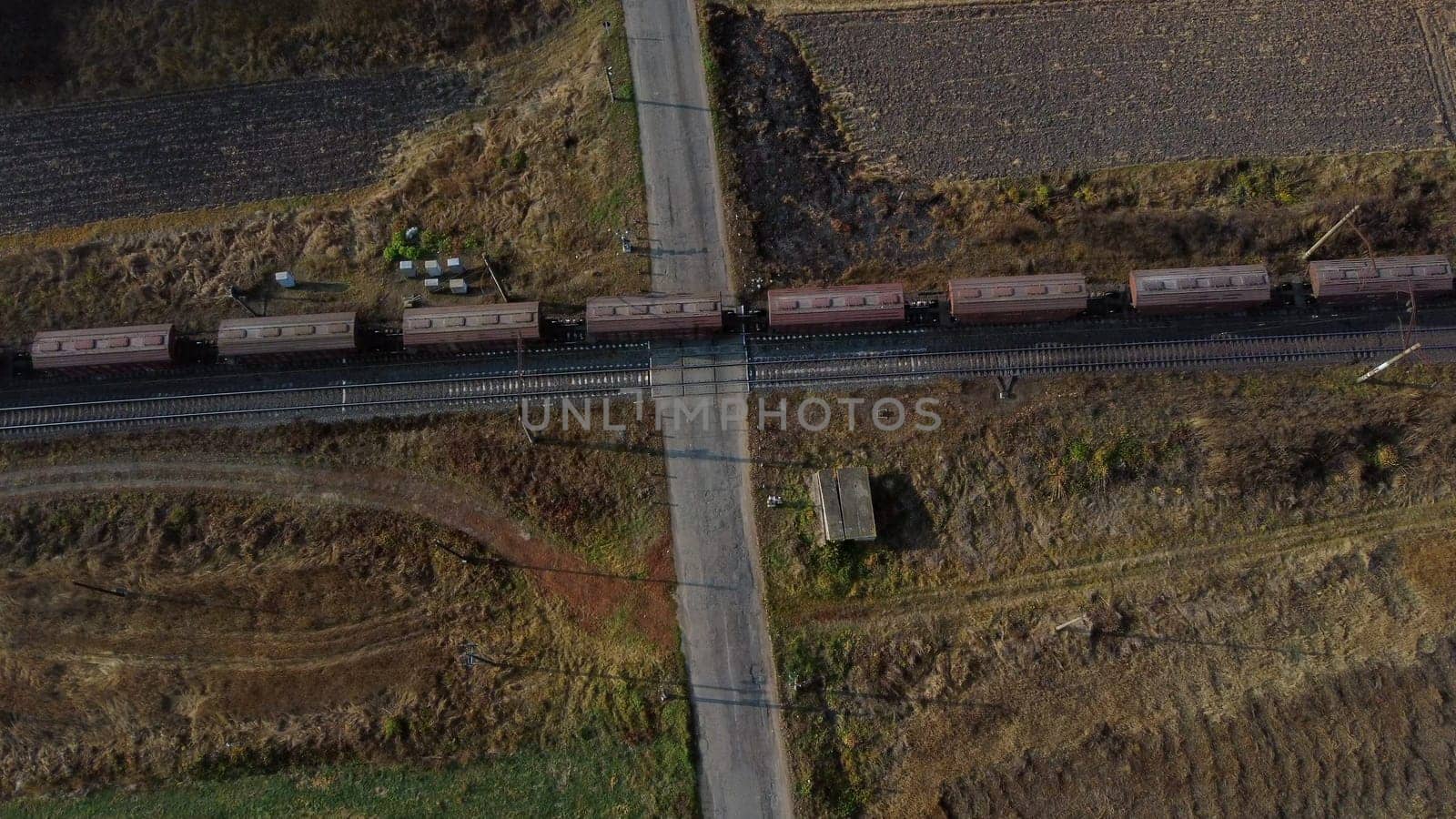 Top View Freight Train Passing Railway Crossing. Aerial Drone View Flight Over Intersection of Railway Tracks and Asphalt Road. Transportation, Rail freight, Delivery. Railway Wagon Rides on Railroad.