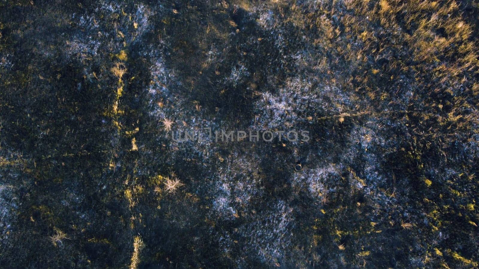 Aerial drone view flight over black ash of field of burned brown yellow dry grass and white smoke on sunny autumn day. View from above. Texture natural background of ecological environmental disaster.