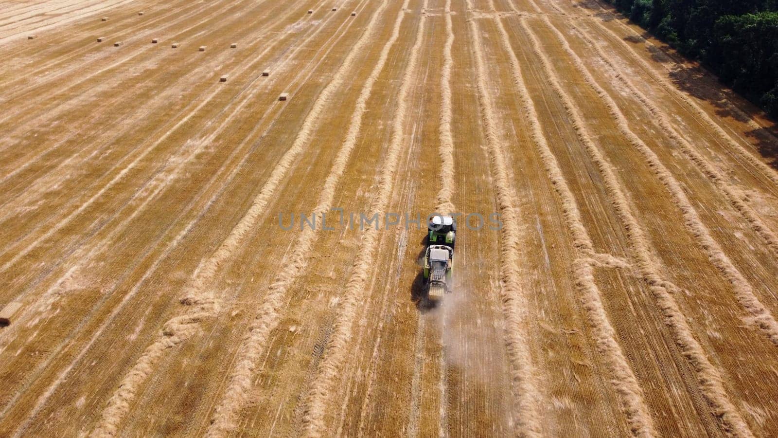 Hay bale tractor. Tractor harvesting hay into bales in field on sunny day. Aerial drone view. Tractor drives across field and makes bales from cut straw. Field and agricultural work, baler. Ukraine