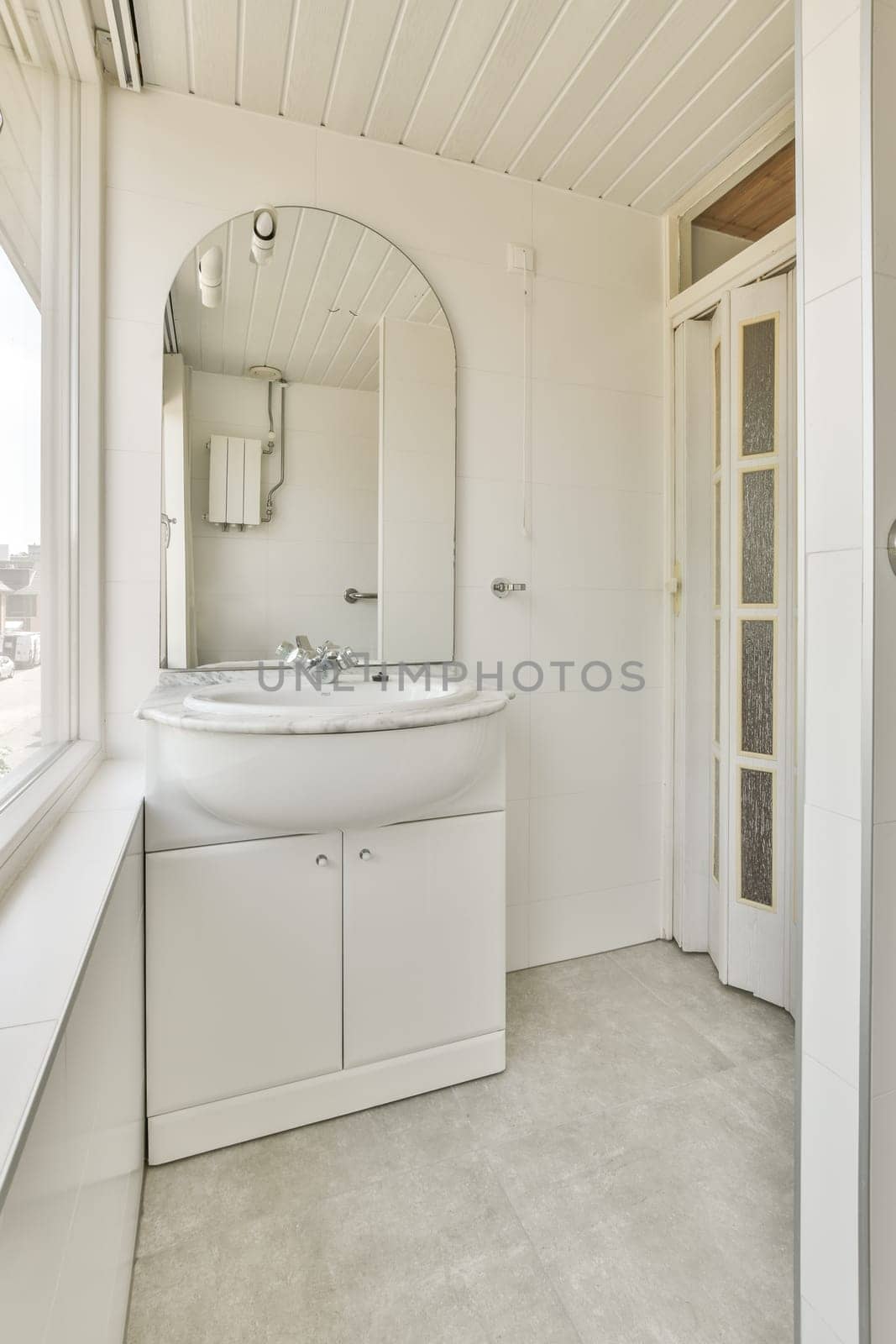 a white bathroom with a sink and mirror in the corner next to an open door that leads to a window