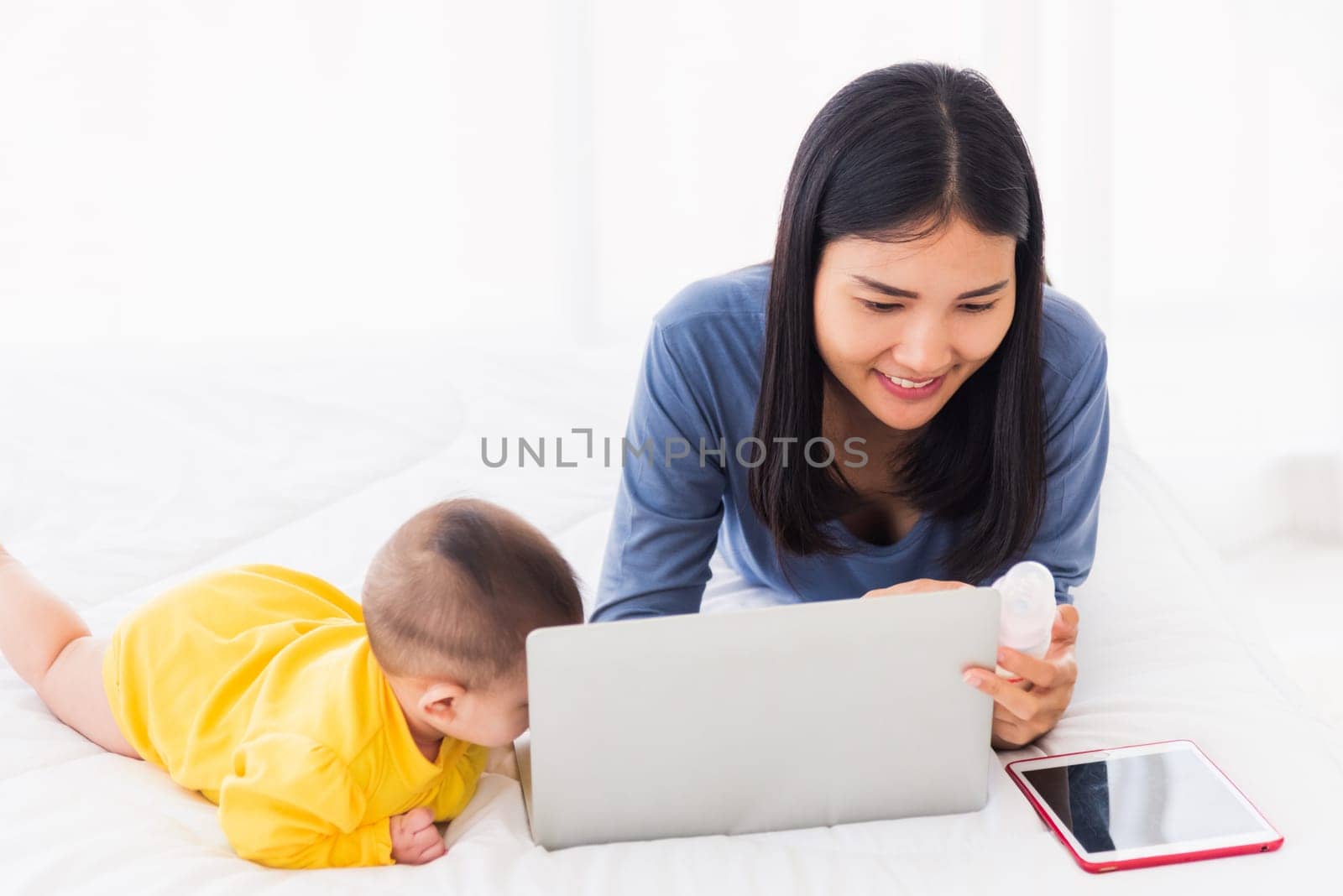 Asian new young beautiful mother finding and reads information on a laptop for milk mixing by Sorapop