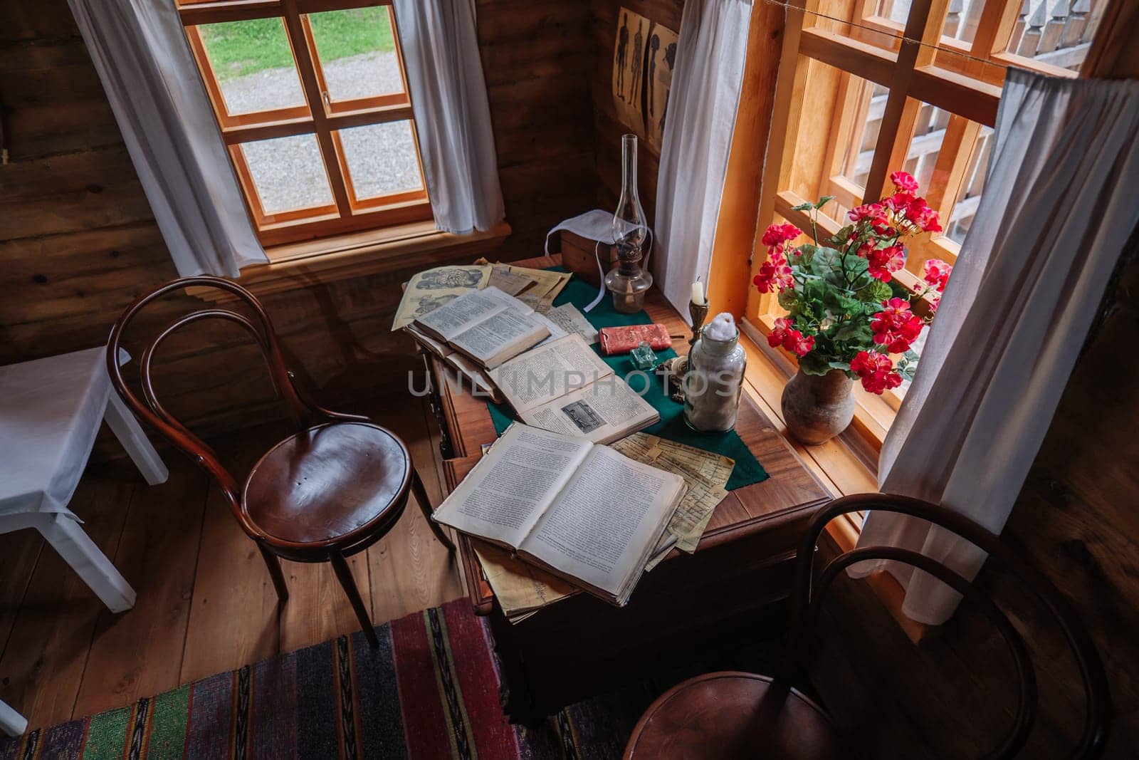 Open books are lying on a desk in a rustic study room illuminated by natural light from a window with red flowers