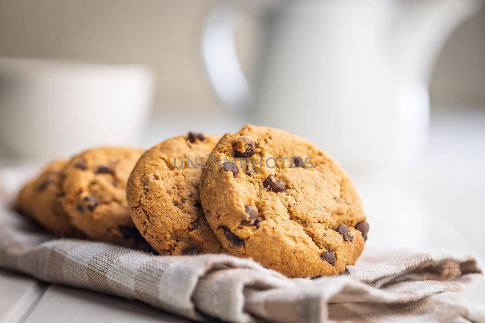 Chocolate chip cookies on napkin on a white table.